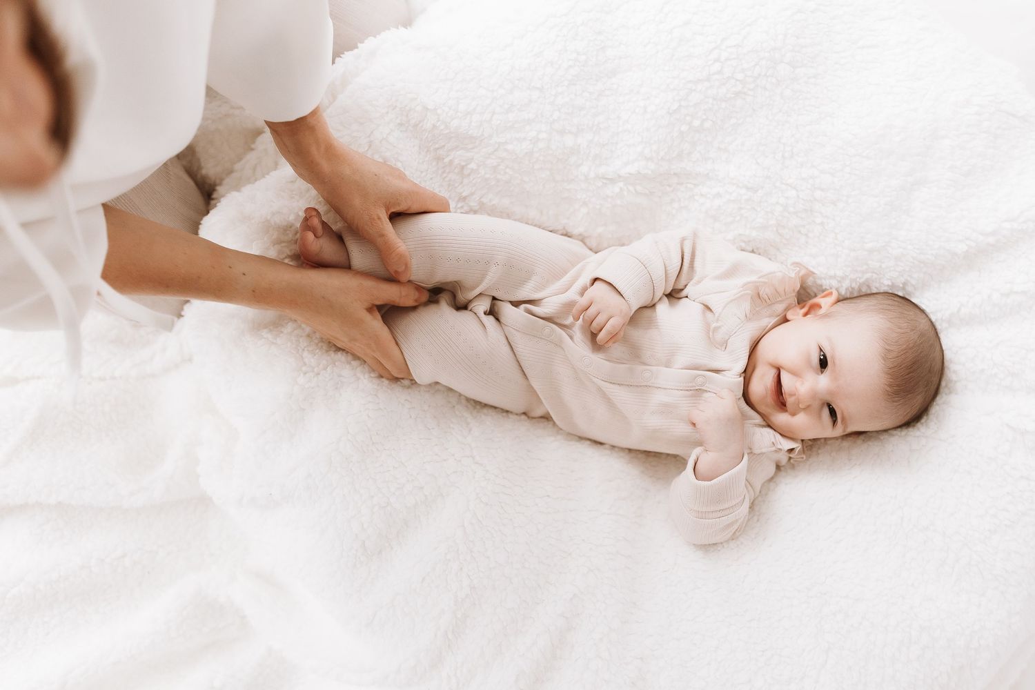 Newborn baby sleeping peacefully on white bedding while being gently touched by adult hands.