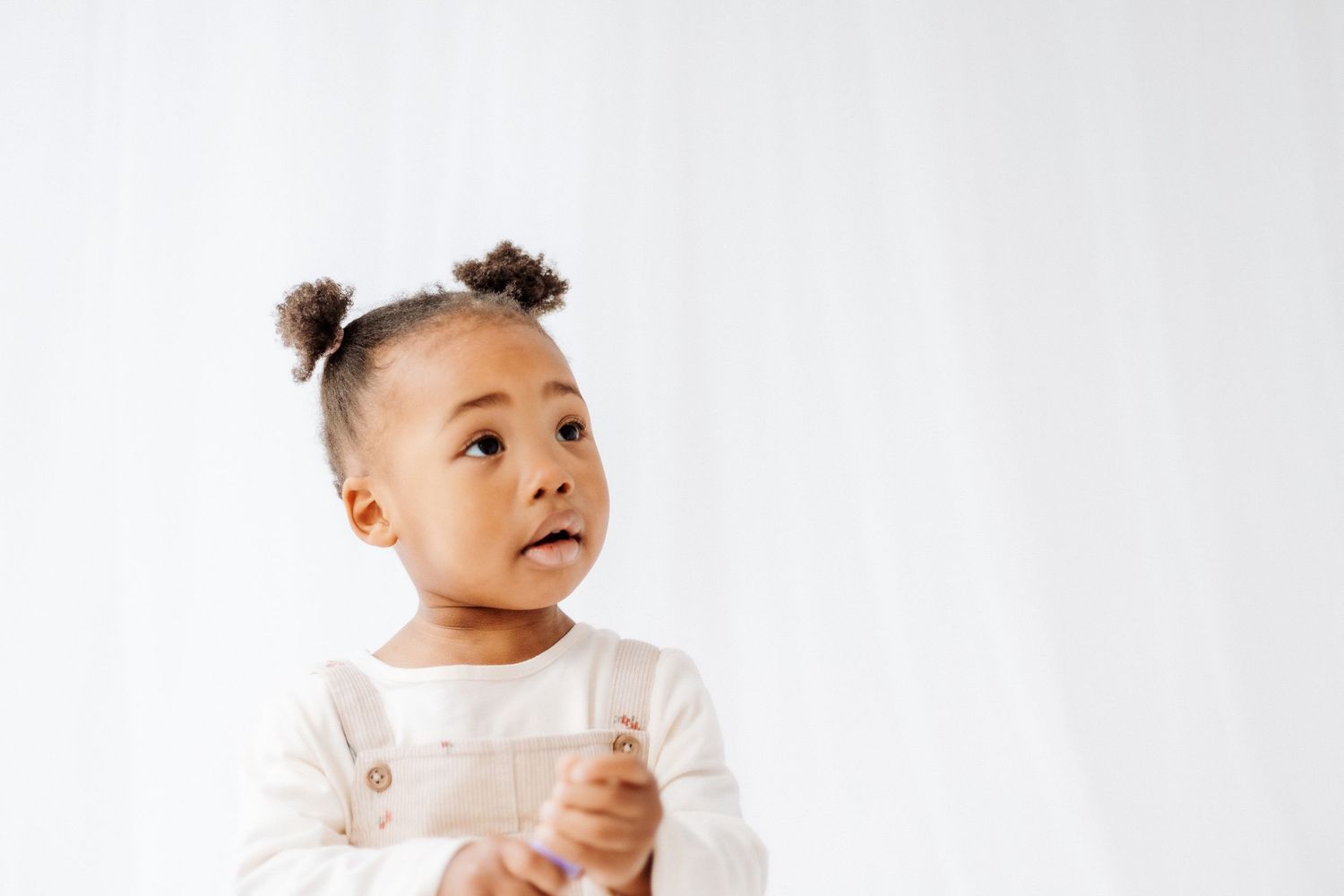 Toddler wearing a white shirt smiles and plays while sitting on a white background. Shepperton Surrey photography studio portrait baby child