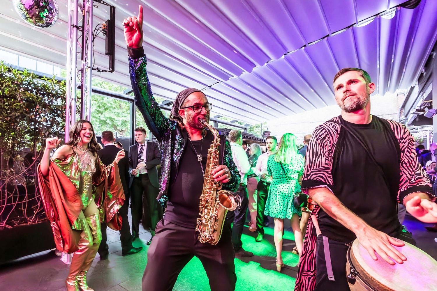 Live band performance with saxophonist and drummer energizing a crowded party venue with colorful lighting.