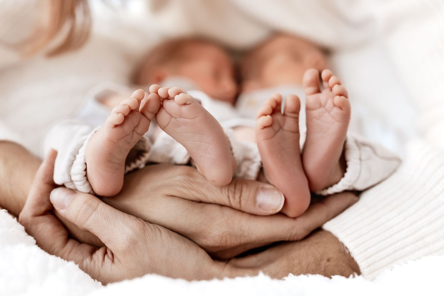 Tiny newborn baby feet and toes lined up in a row on white blanket background.