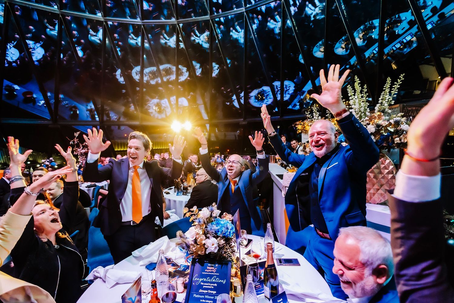 The gherkin London award ceremony Guests celebrating r, raising hands joyfully under dramatic venue lighting.