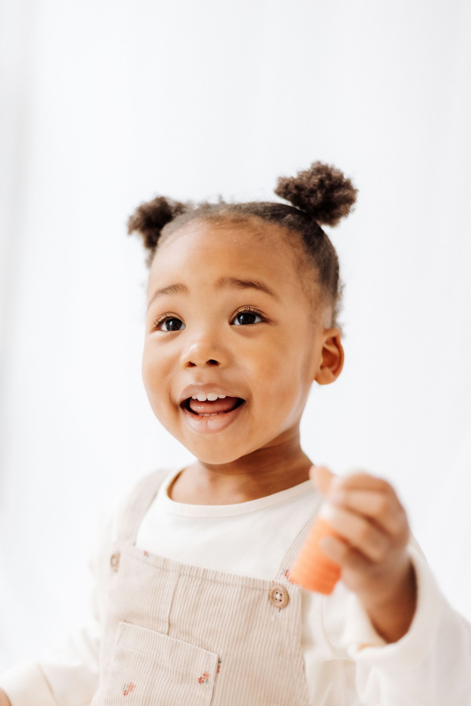 Smiling baby wearing a white top and beige overalls poses against a white background in three sequential photos.