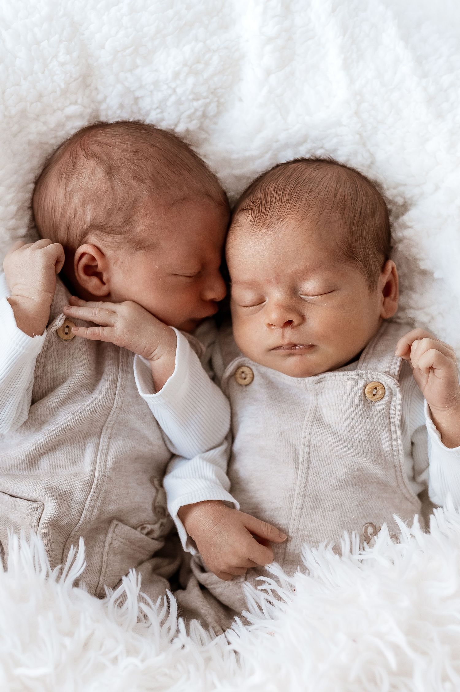 Three sleeping newborns lie side by side on soft white bedding in a tender and peaceful moment.