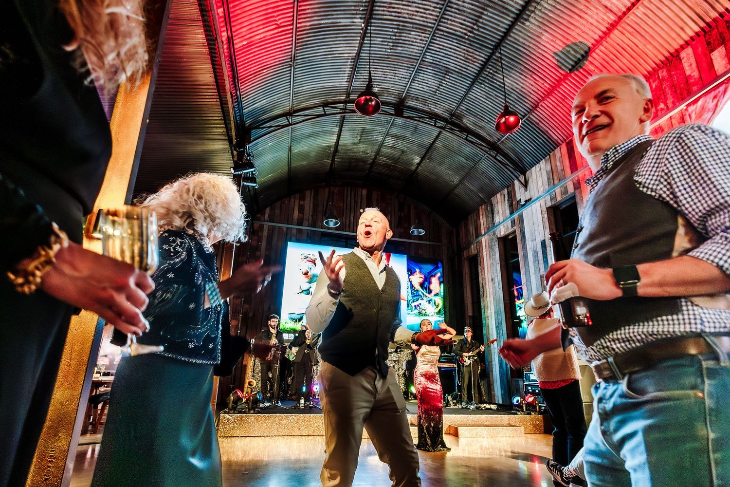 Joyful guests dancing and laughing at a lively indoor event venue with colorful stage lighting.