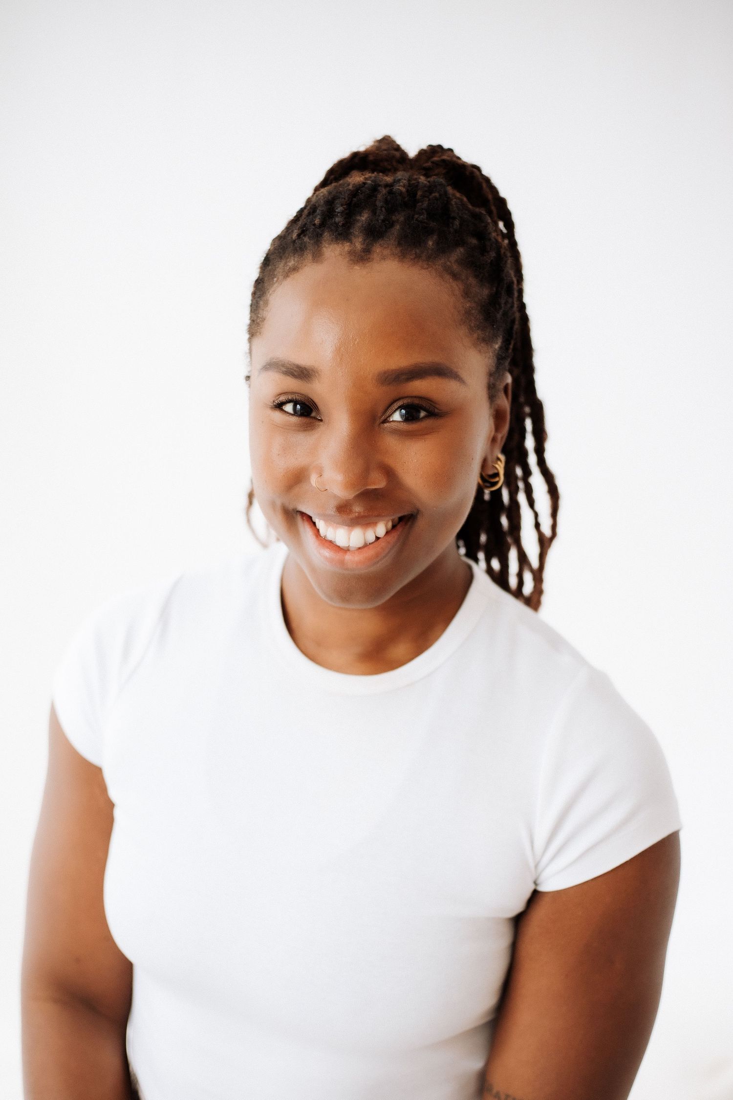 A person wearing a white t-shirt smiles warmly against a light background.
