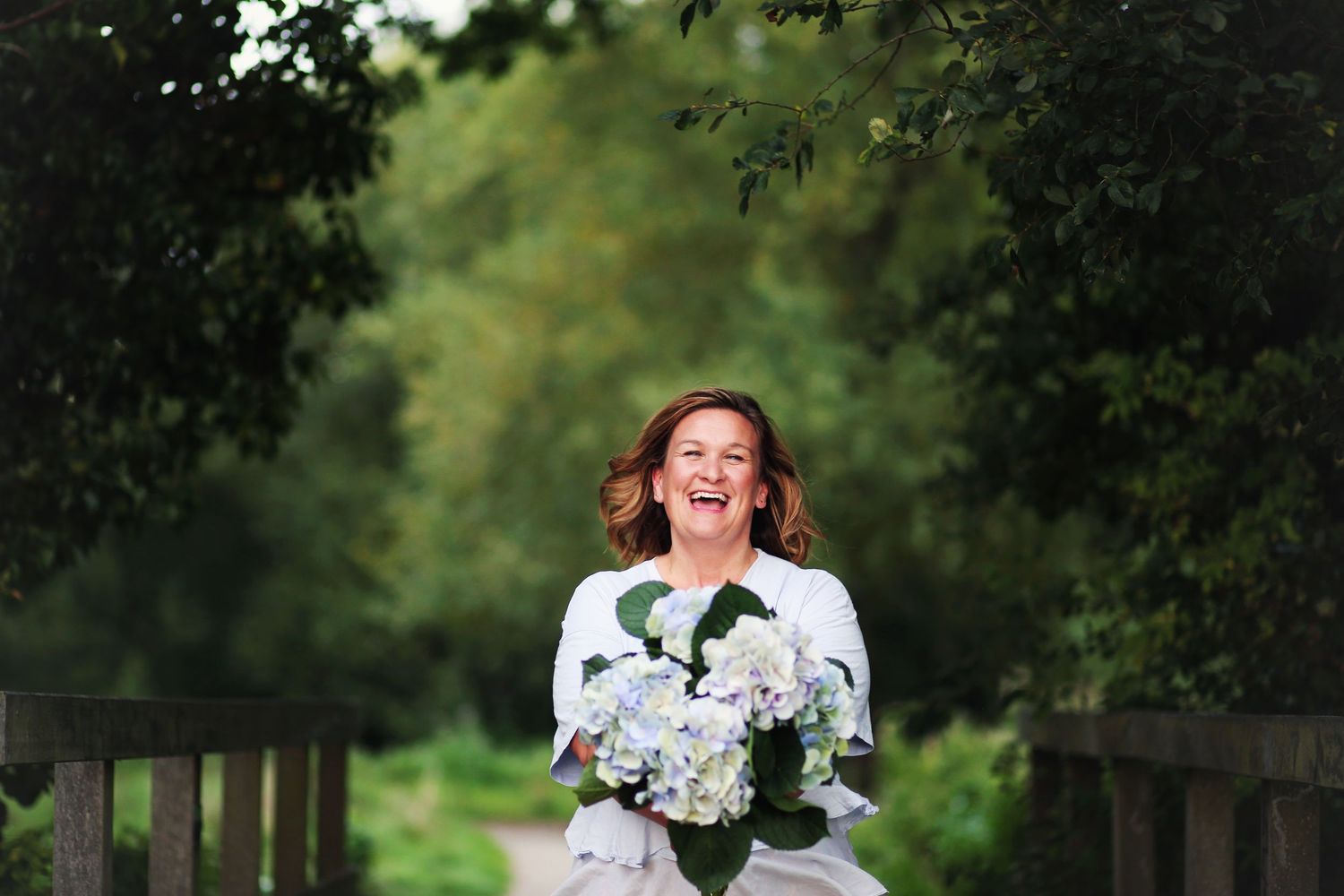 A person in a white dress with black accents poses joyfully in a lush garden setting.