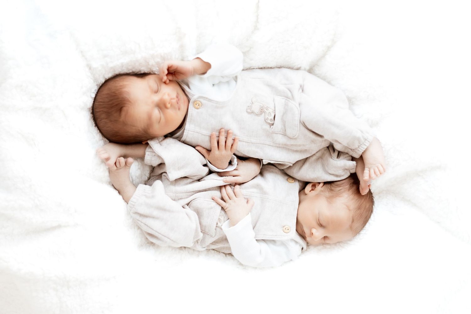 A baby wrapped in white fabric lies on a white surface, creating a soft and serene portrait.