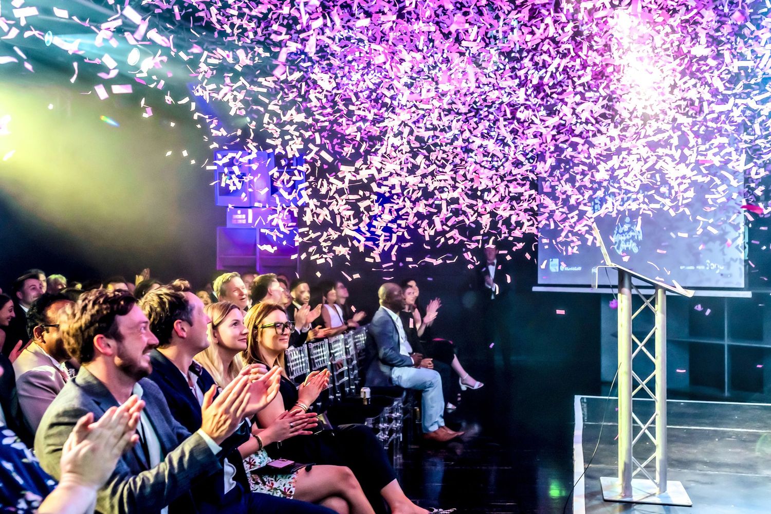 Ministry of Sound London. Crowd celebrating with purple confetti at a lively event, clapping and cheering under colorful stage lighting
