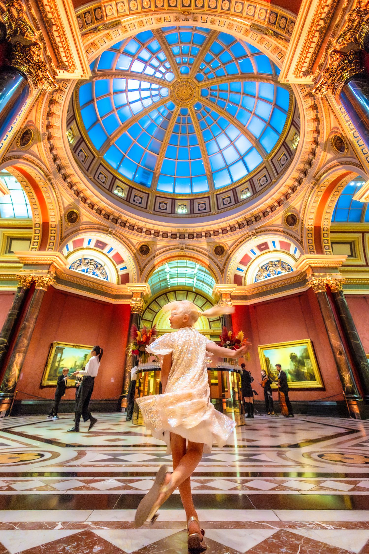 Woman dancing in ornate museum hall with stunning blue stained glass dome ceiling and colorful arched walls.