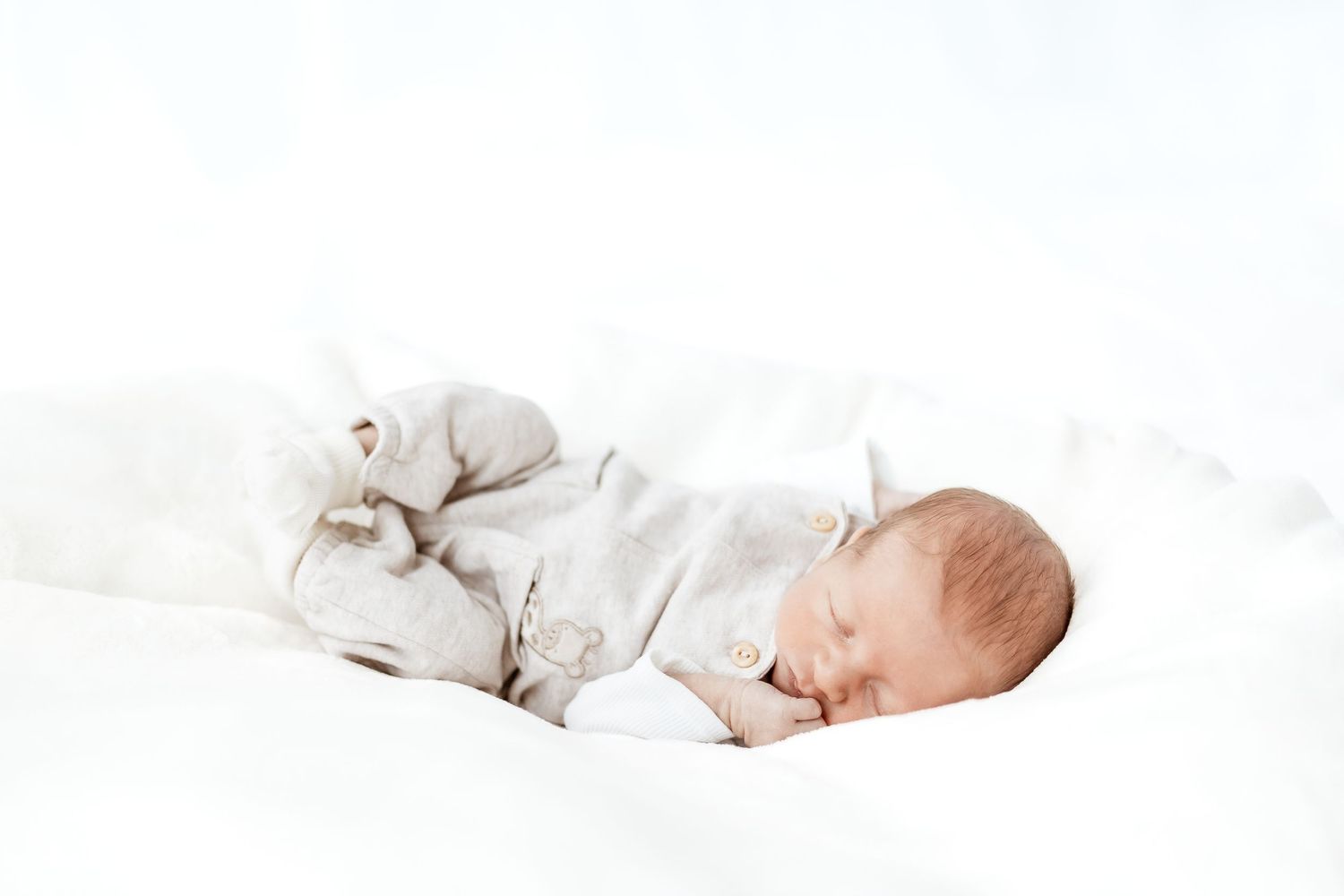 Two sleeping babies dressed in light colored clothing lying on white blankets.