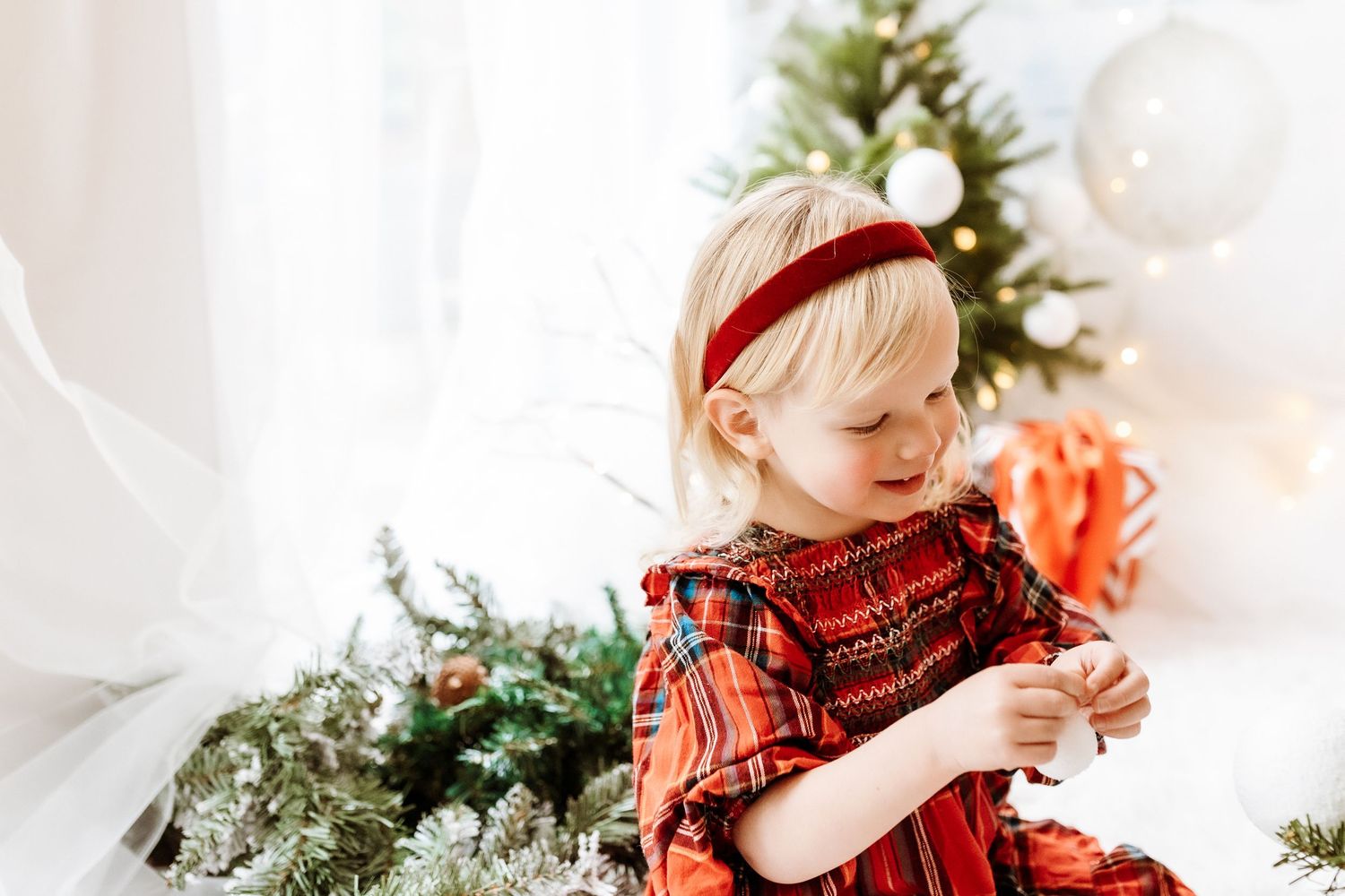 A child in red plaid clothing reaches up to decorate a Christmas tree with ornaments and lights.