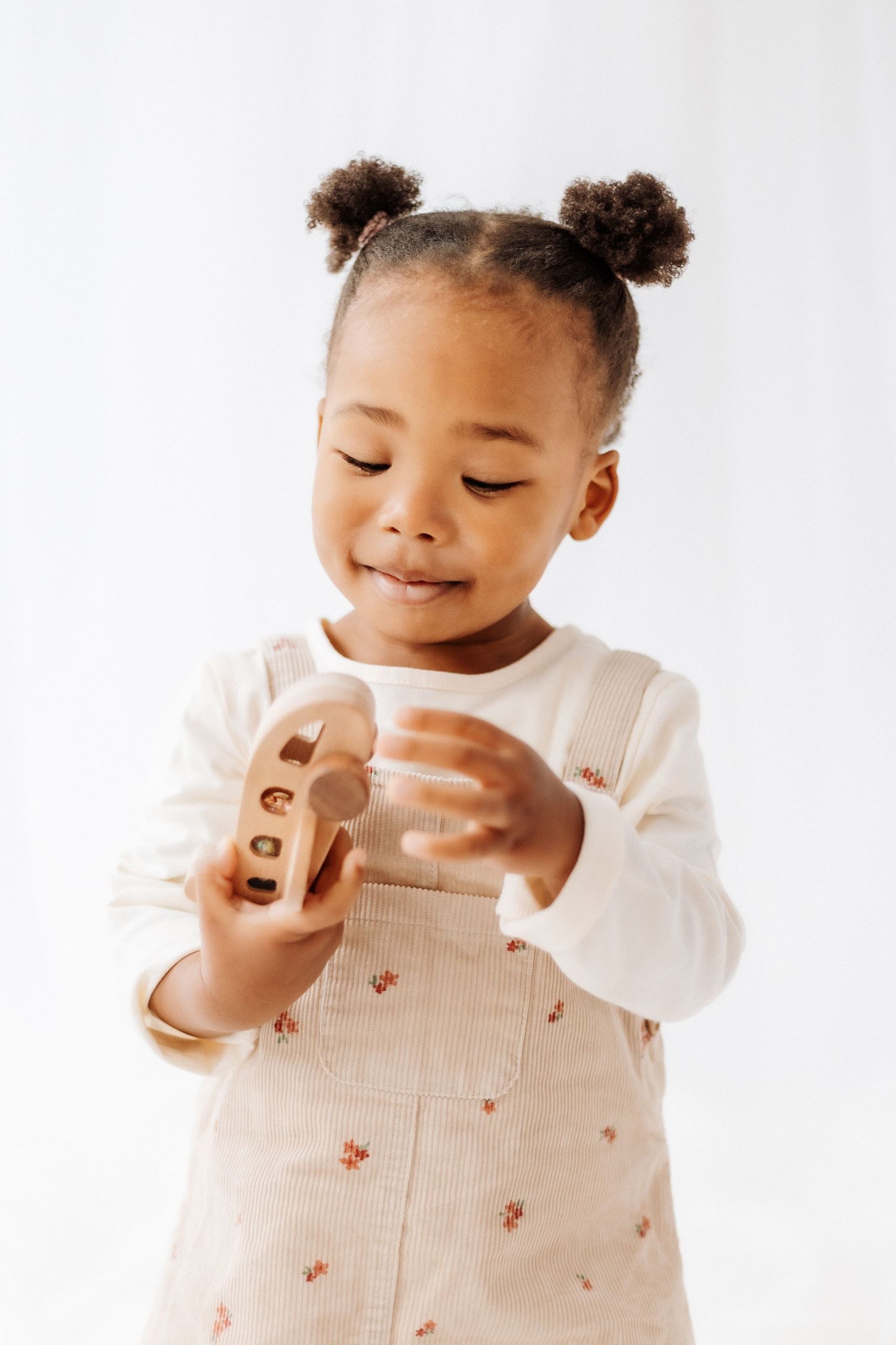 Toddler in white shirt plays with wooden toys against light background showing joyful expressions. Shepperton Surrey photography studio