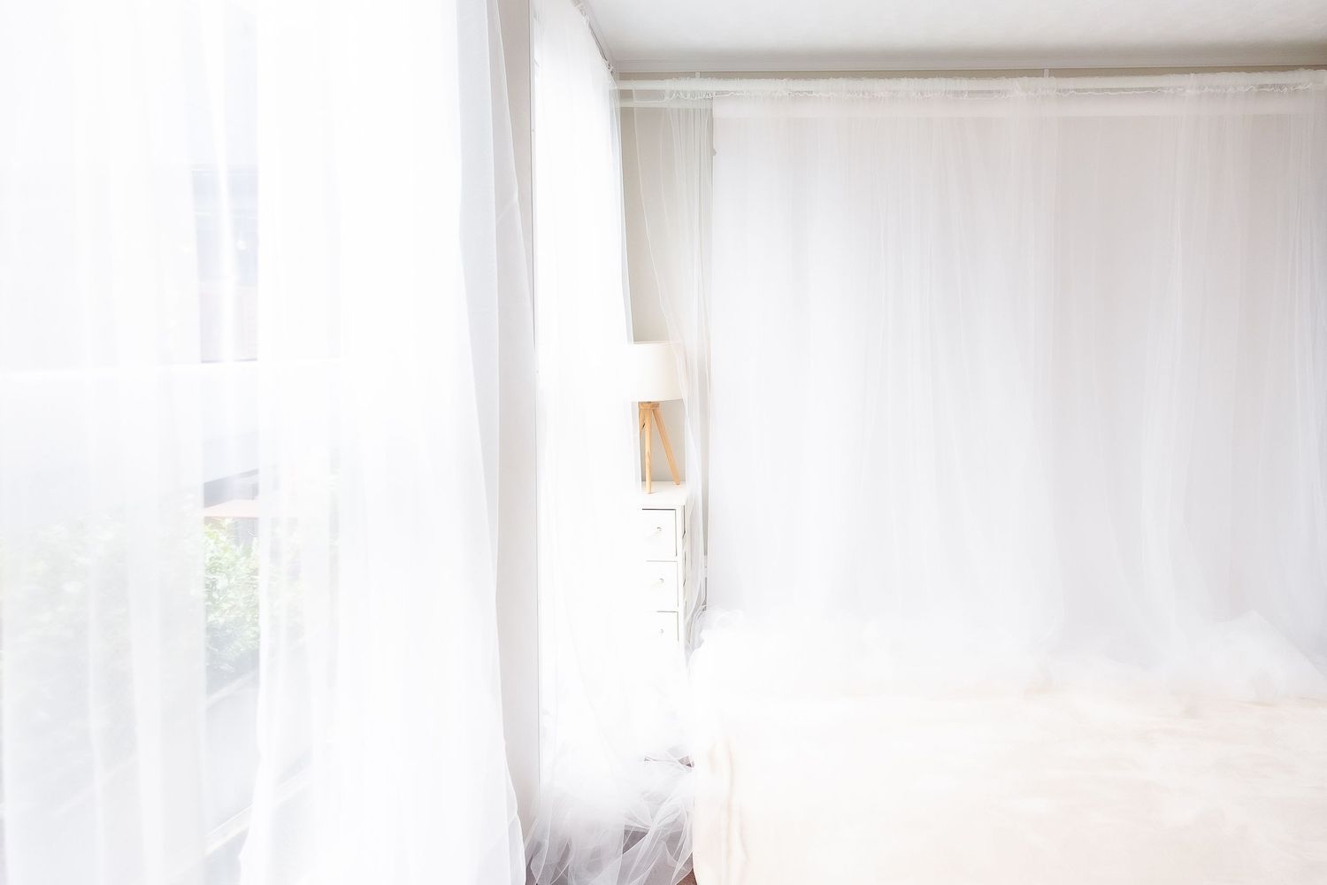 Bright white interior corner of a room with sheer curtains letting in natural light through a window.