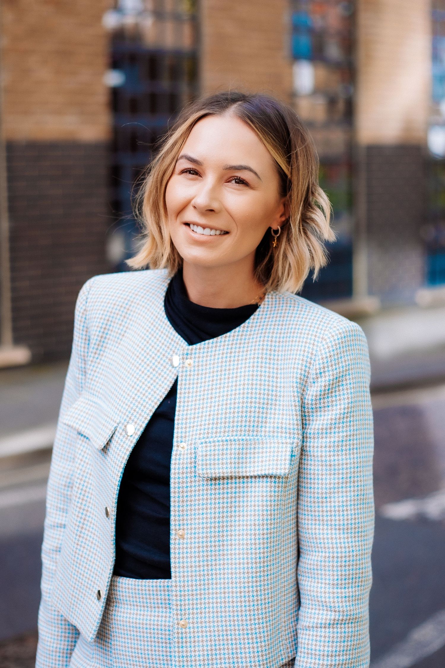 Professional portrait series showing a light gray checkered blazer styled with a black top against an urban backdrop.