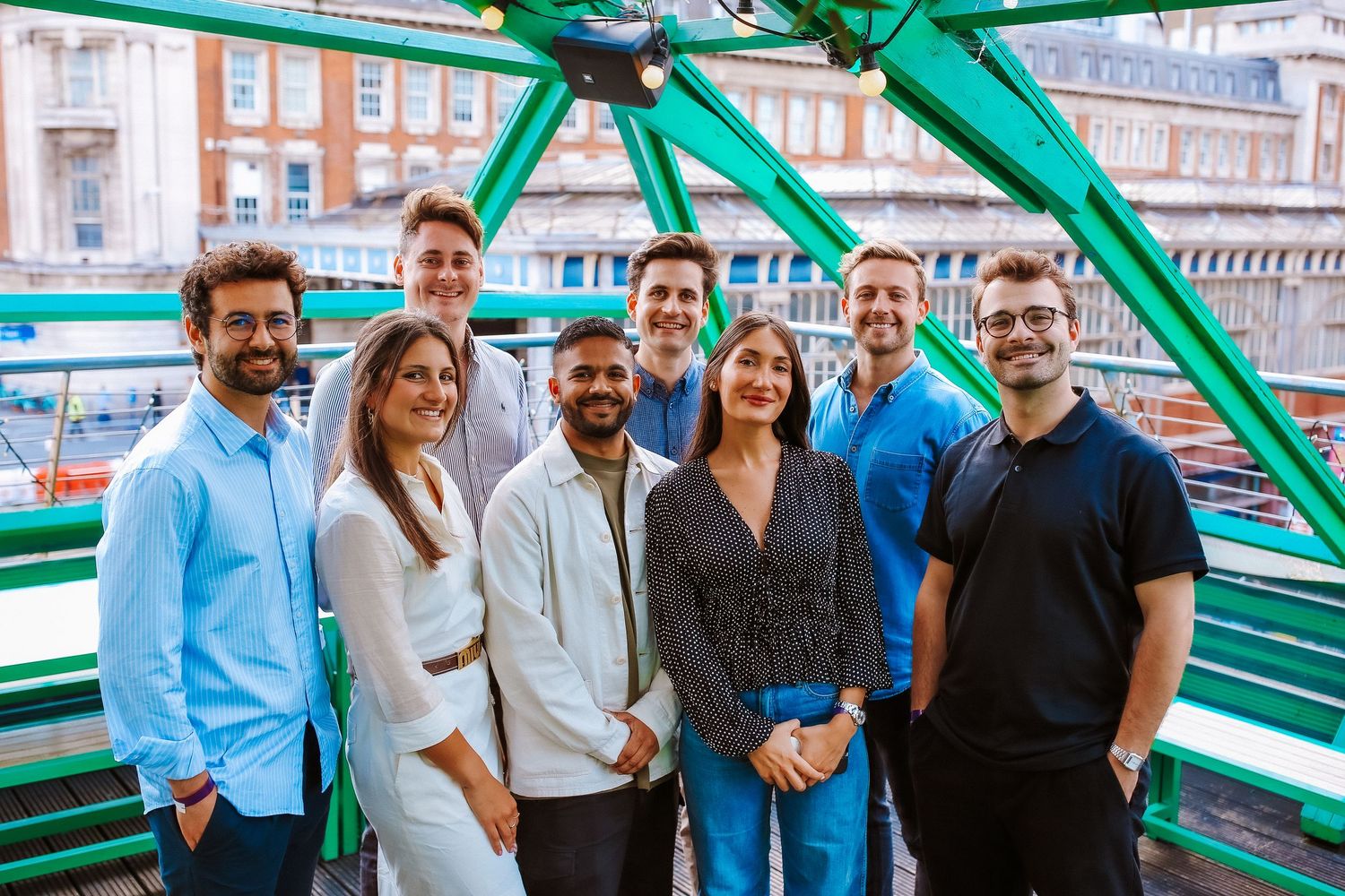 A group of professionals stand together smiling on a green bridge structure in an urban setting.