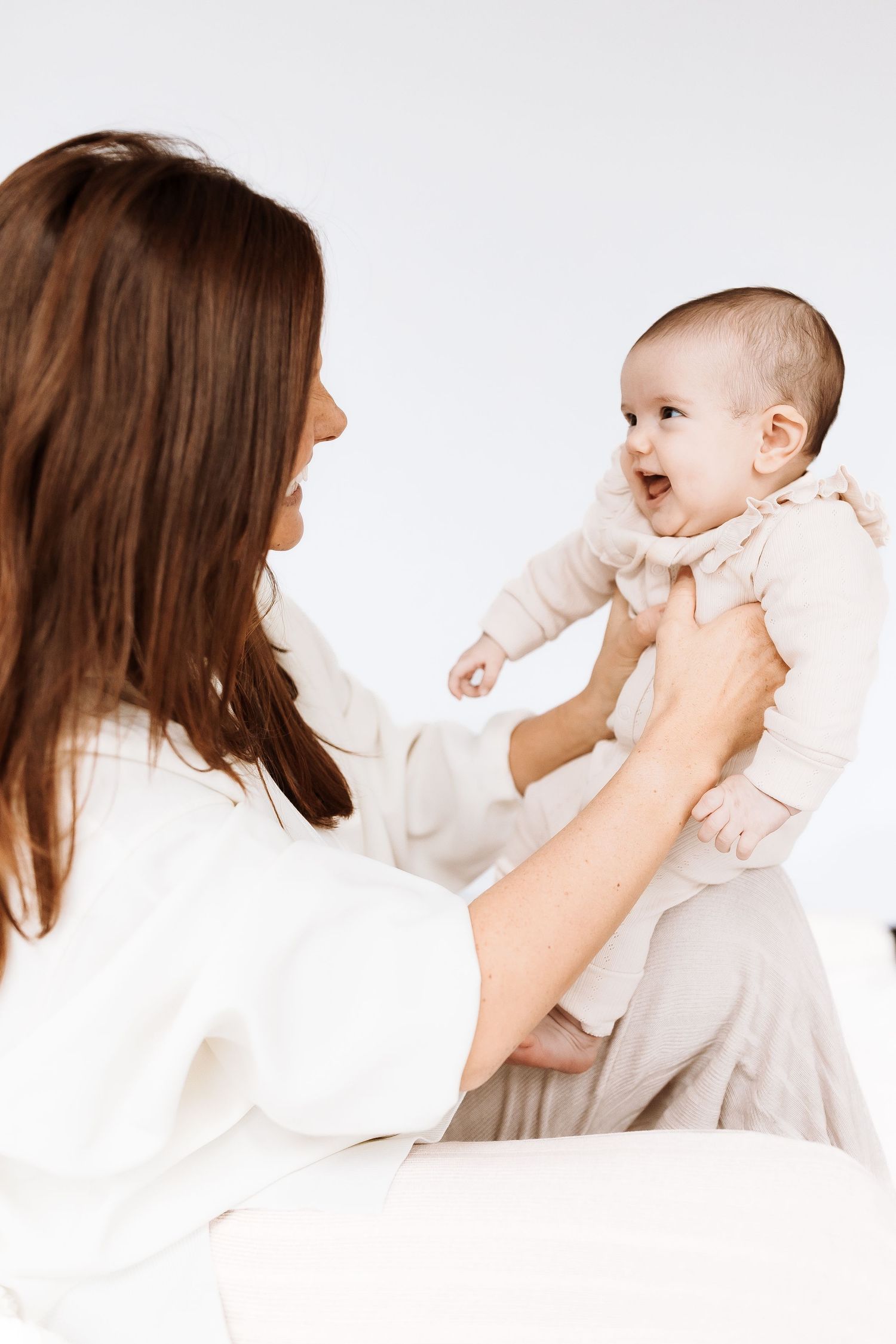 Parent and baby laughing together against a minimalist white background. candid photography baby, family Shepperton Surrey studio
