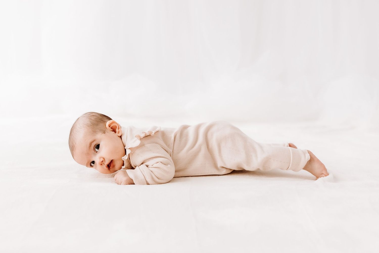 A baby in white clothing lies on a light background in three different poses. candid photography baby, family Shepperton Surrey studio