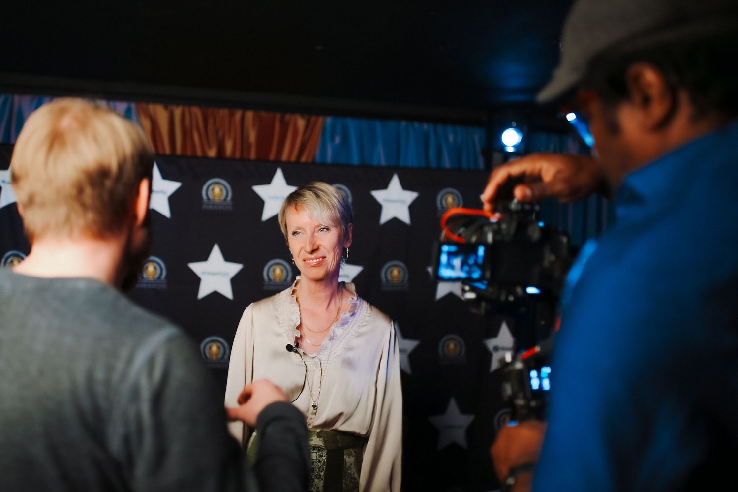 Woman being interviewed on camera in front of a star-patterned backdrop at a media event. award ceremony interview photography
