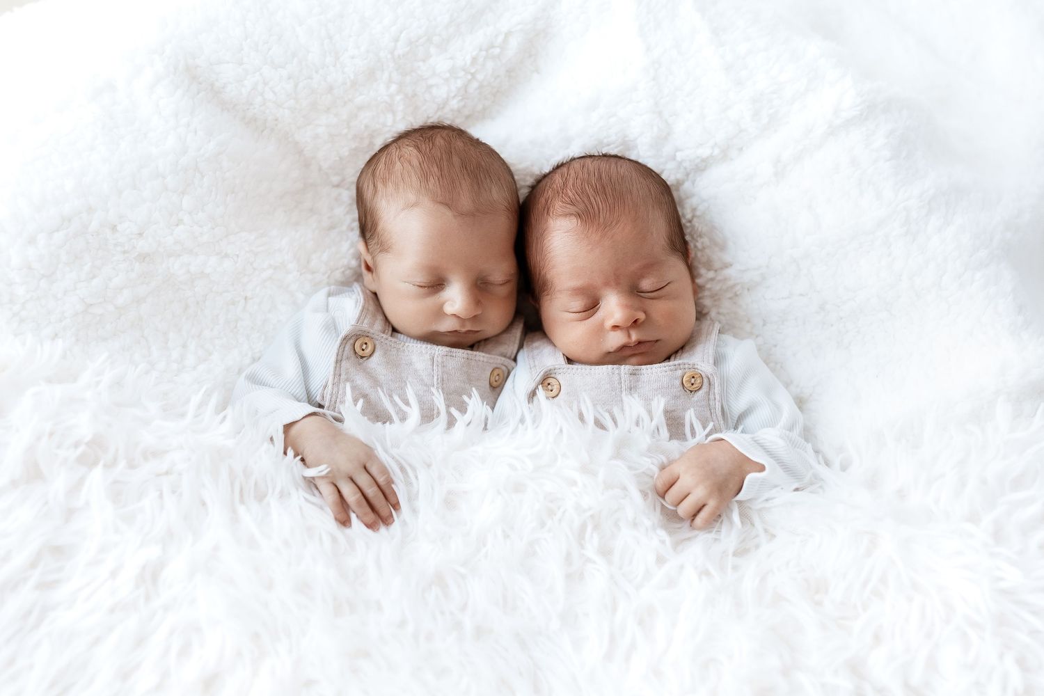 Sleeping twin babies cuddled together on white textured blanket.