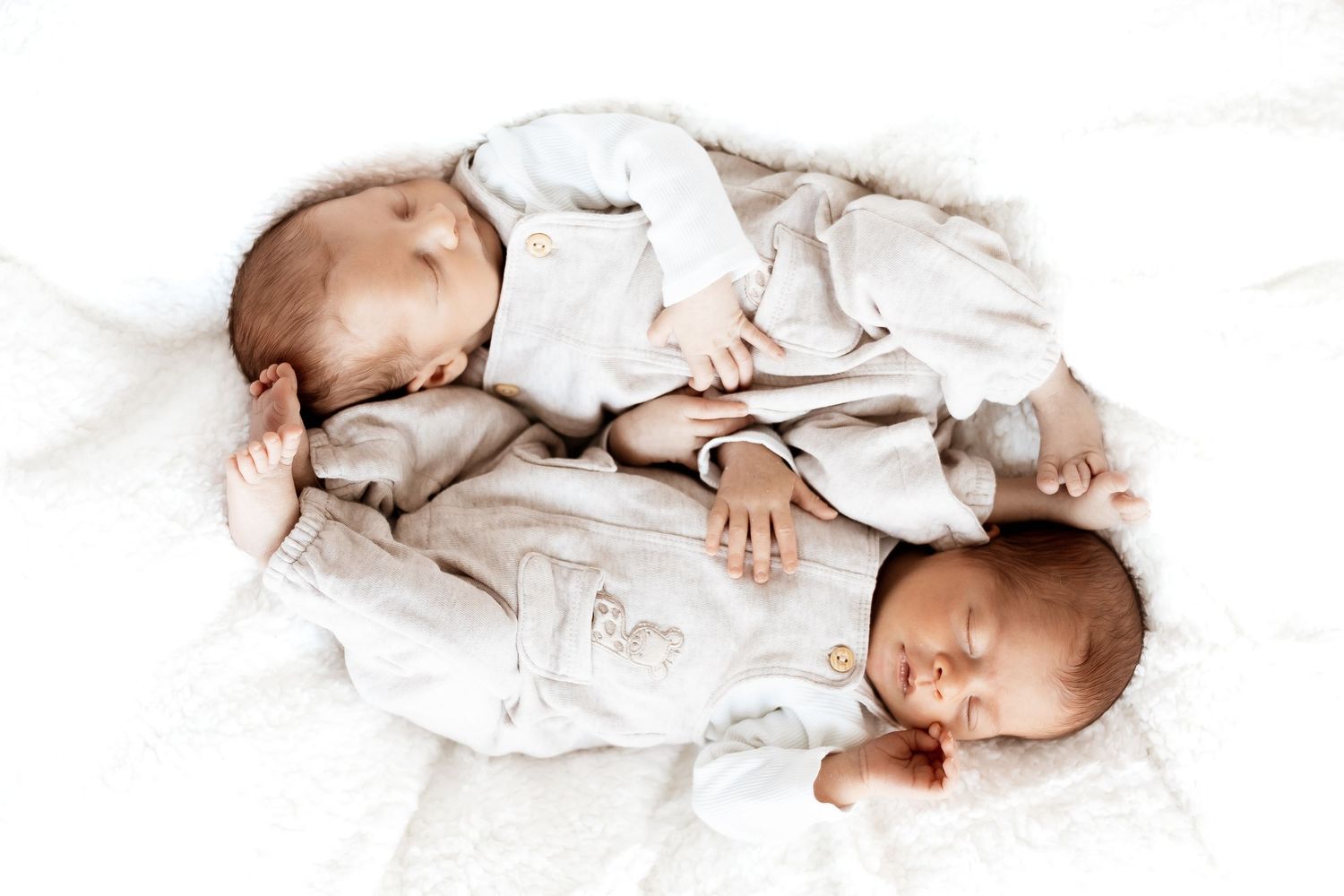 A baby in a white outfit lies on a white background, creating a minimalist portrait composition.