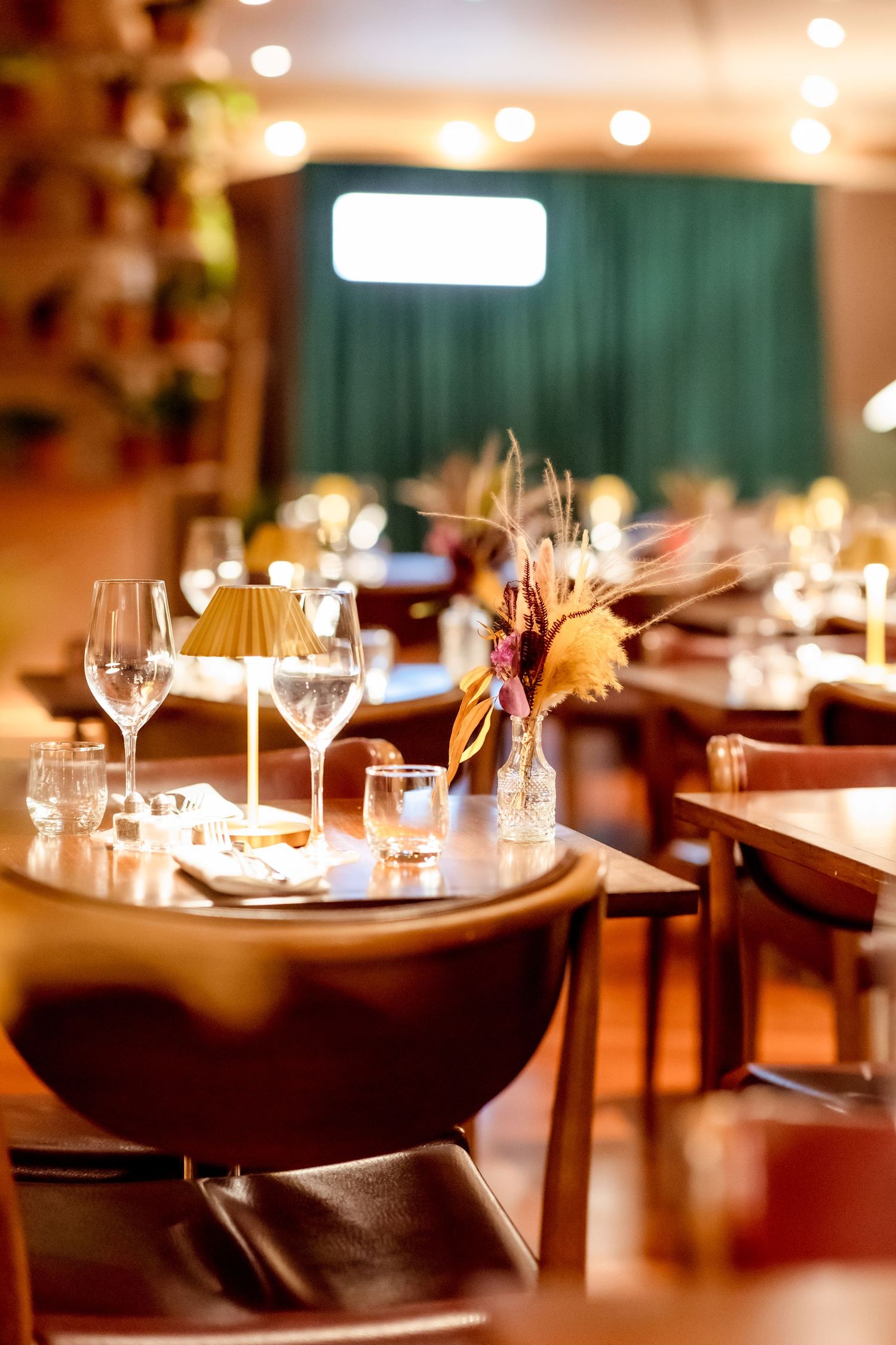 Elegant restaurant interior with set tables, wine glasses, warm lighting, and floral centerpieces in a cozy dining atmosphere.
