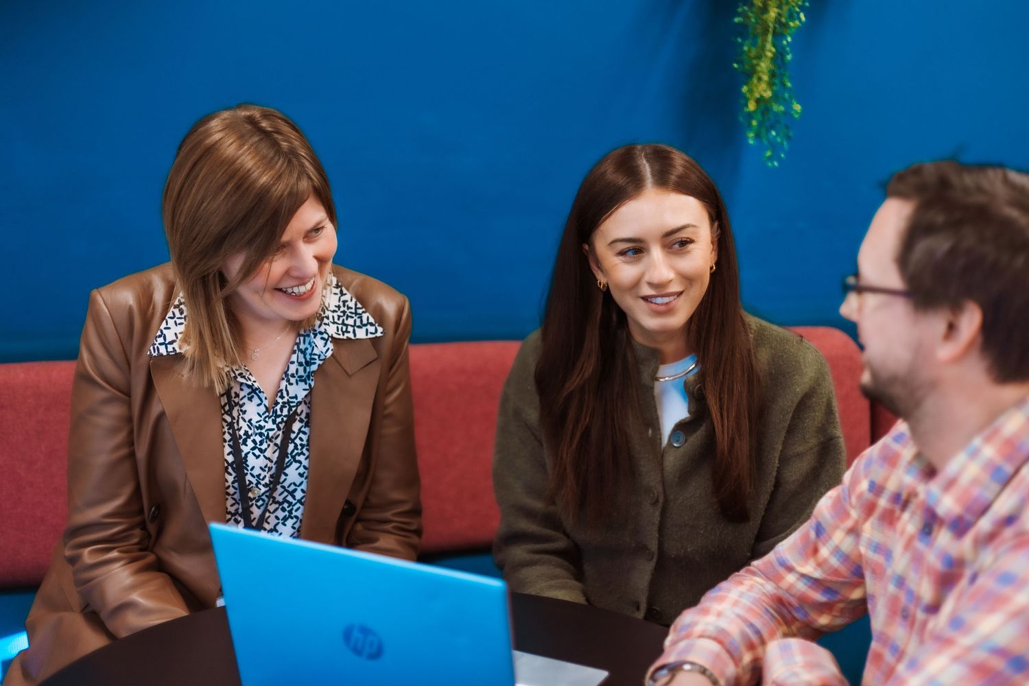 A group of people in business attire collaborating and discussing ideas around a laptop in a modern office setting.