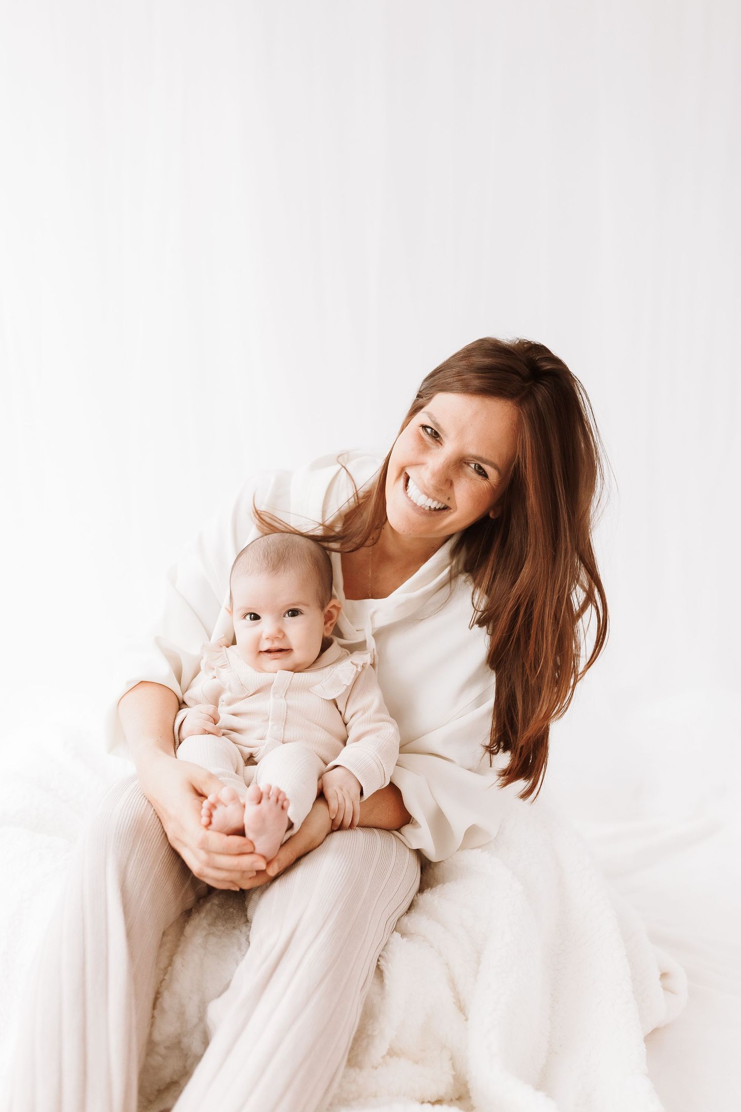 A mother and baby share tender moments in a bright white studio setting, creating a heartwarming series of interactions.