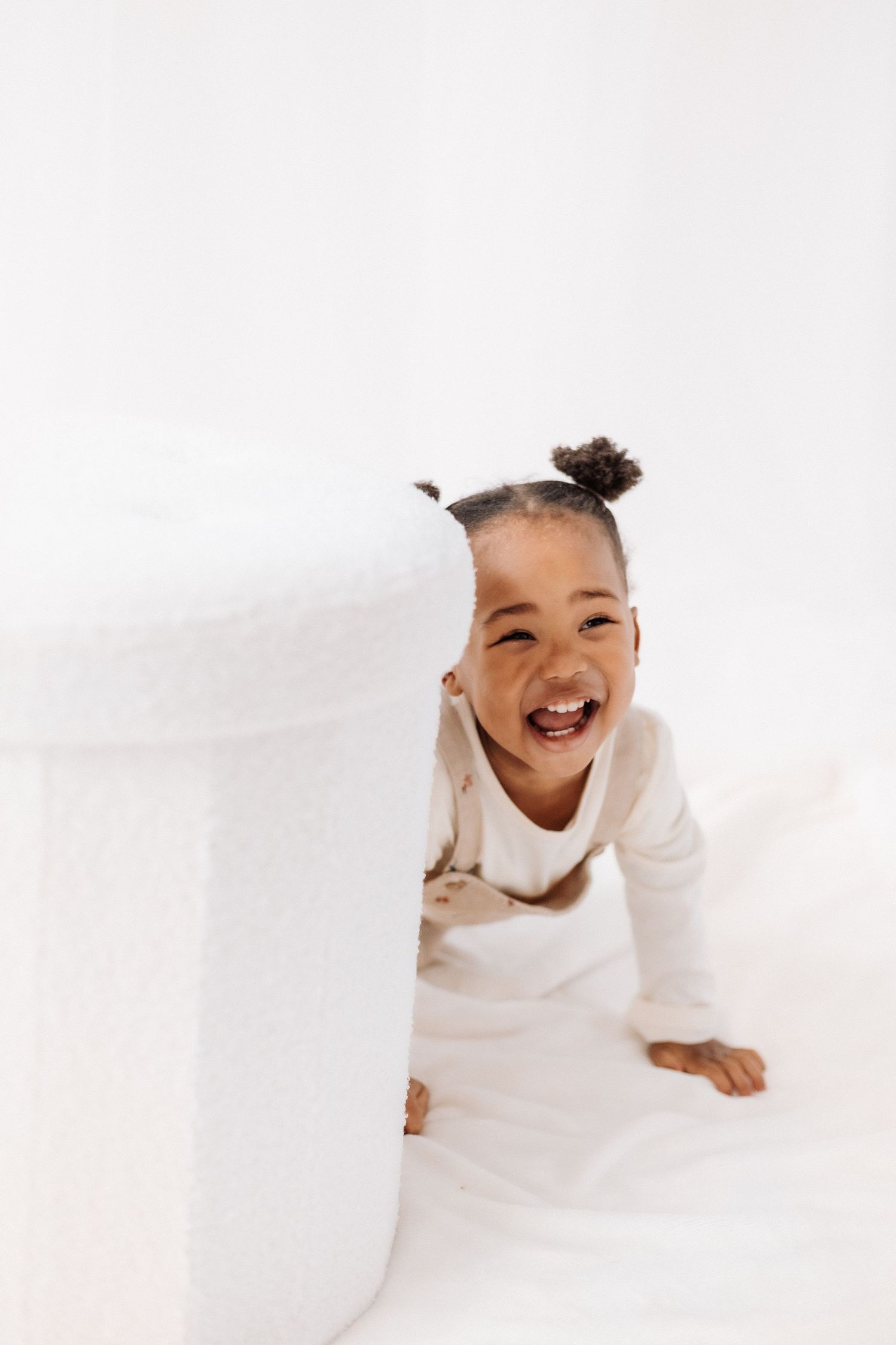 Child laughs while lying down against a white background.  Shepperton Surrey photography studio portrait baby session