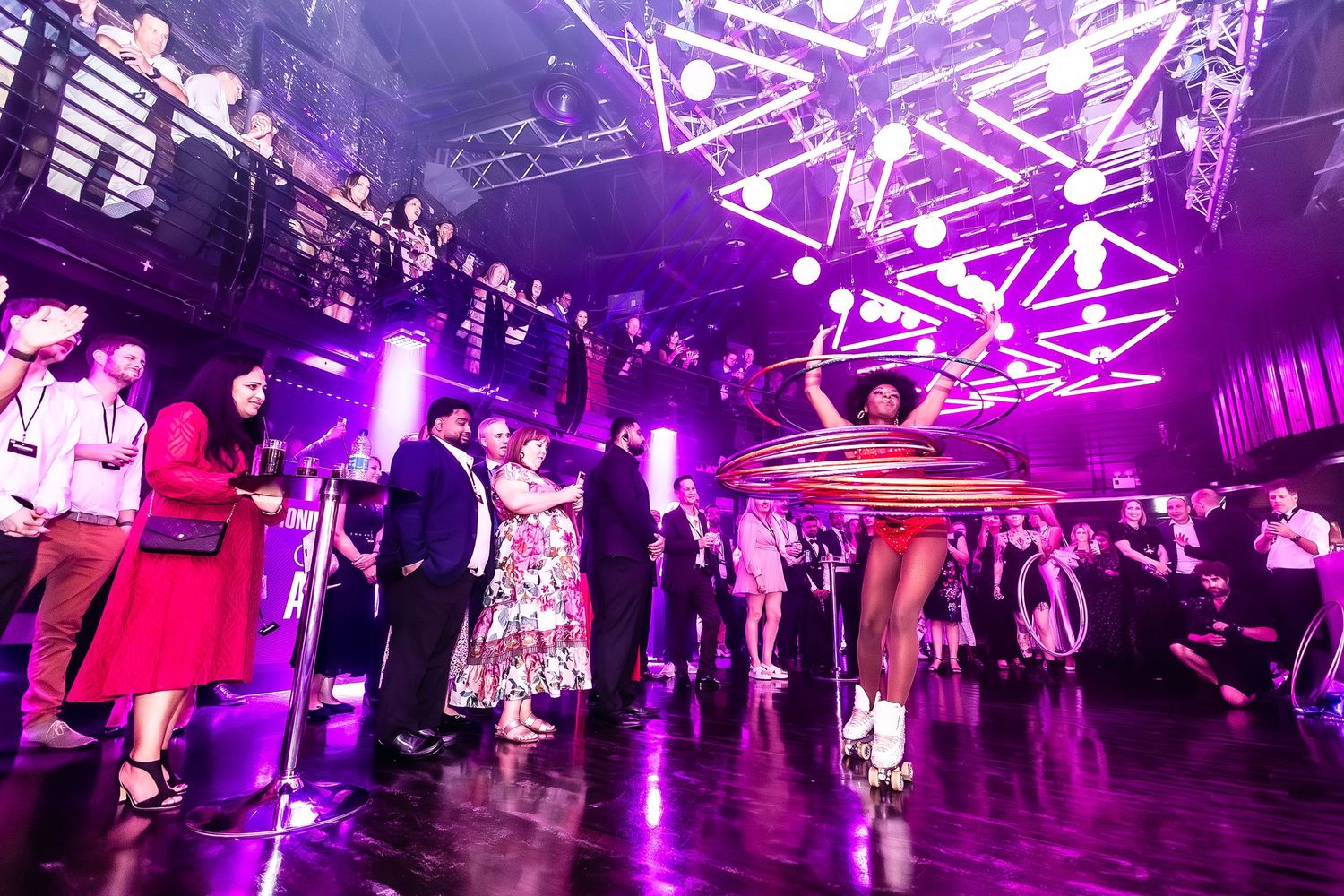Ministry of Sound London nightclub event with performers, hula hoop dancer, and guests under purple lights and decorative ceiling rigs.