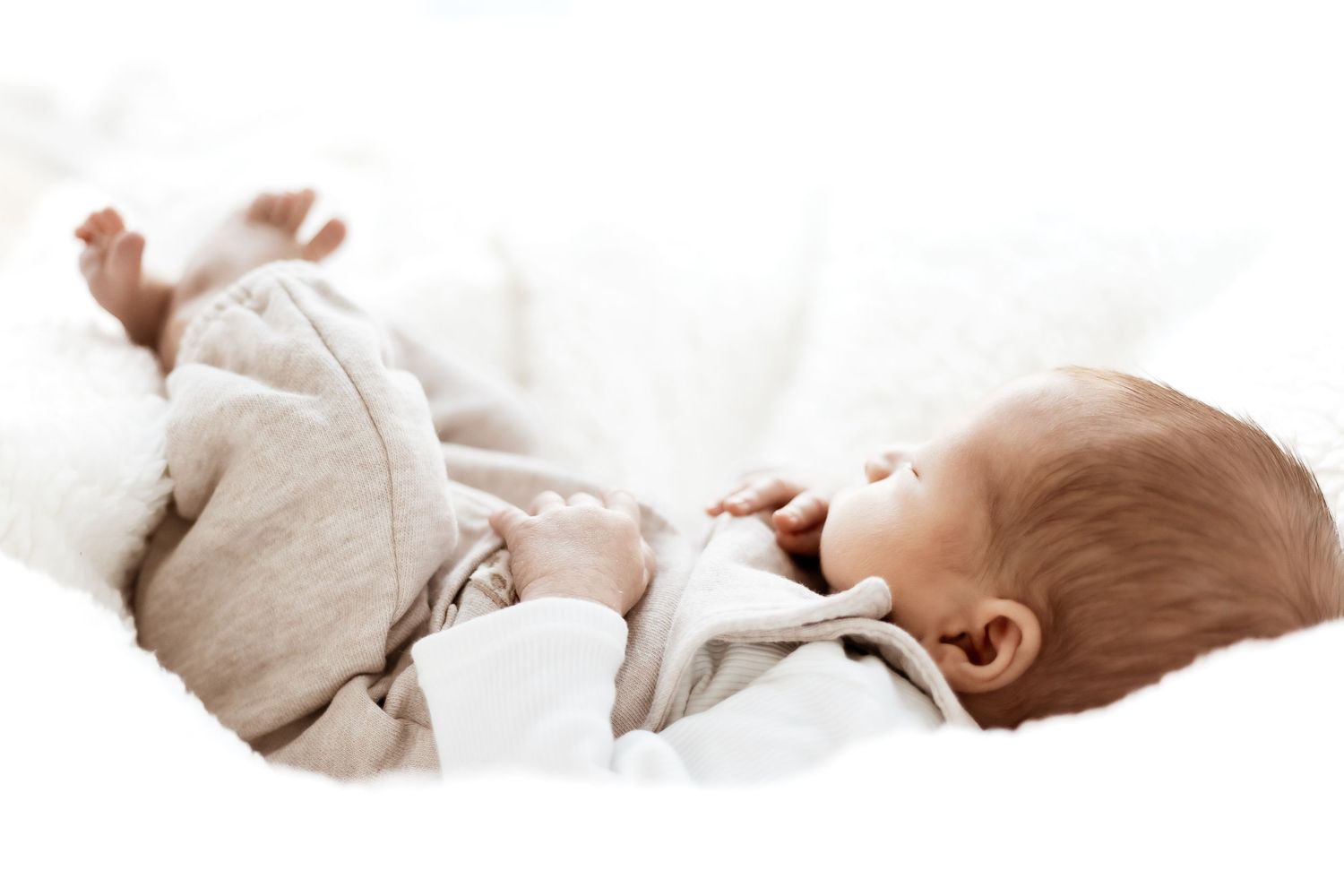 A sleeping baby lies peacefully in soft white bedding with a gentle natural light illuminating the scene.