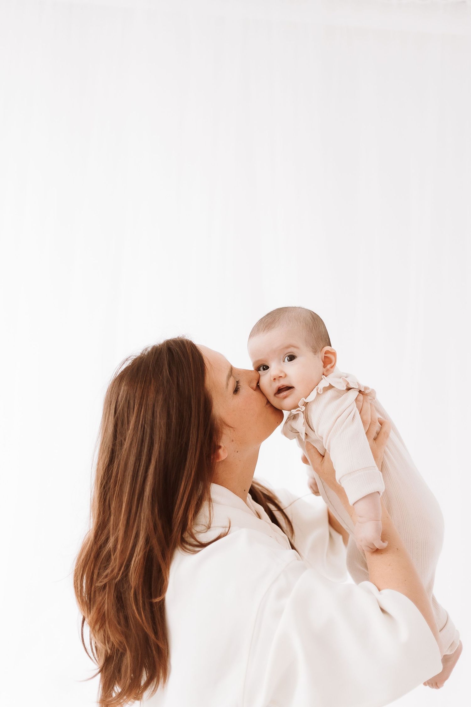 A series of photos showing tender moments between a parent and baby in white clothing against a light background.