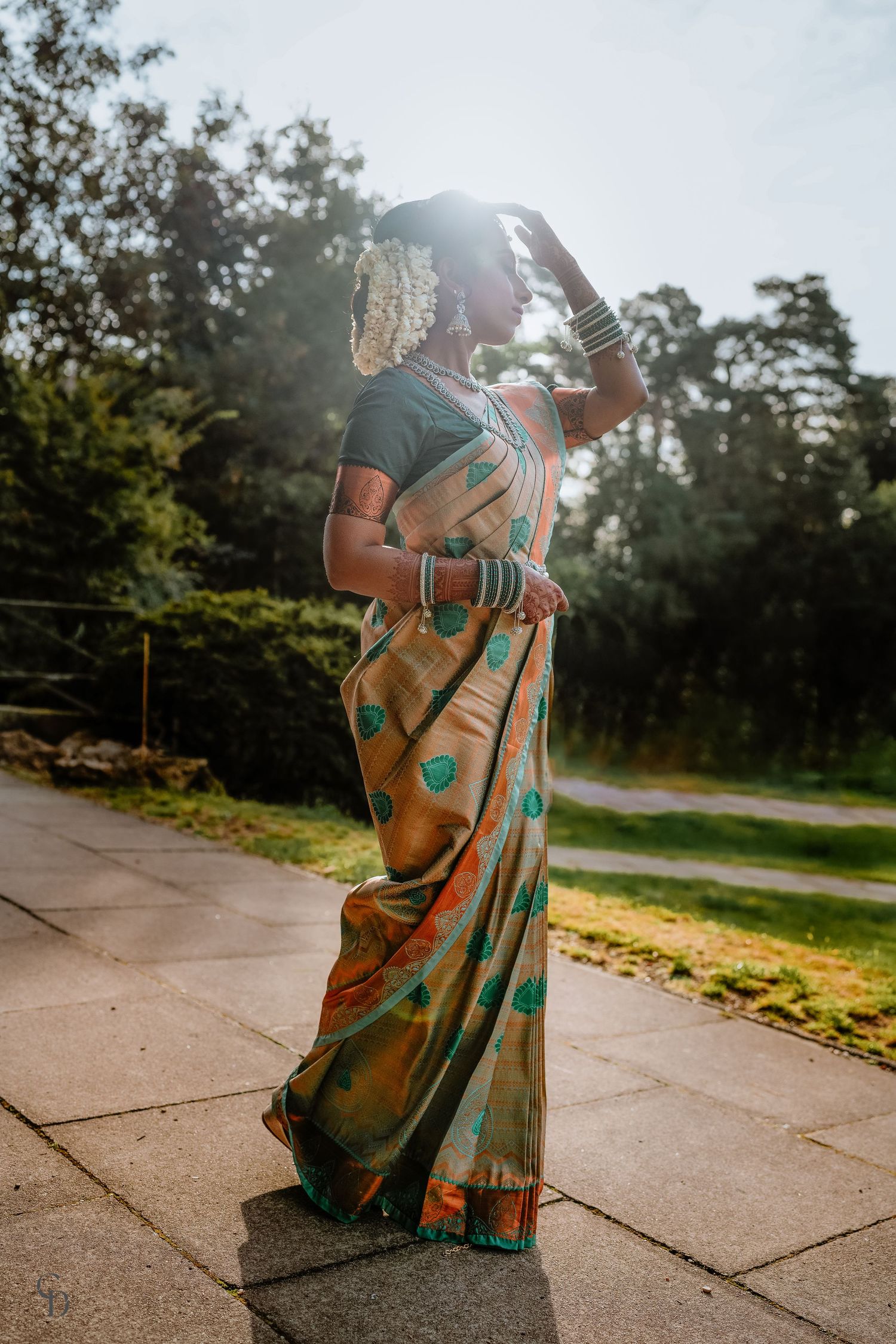 Elegant teal and orange saree photographed against sunlit outdoor setting.