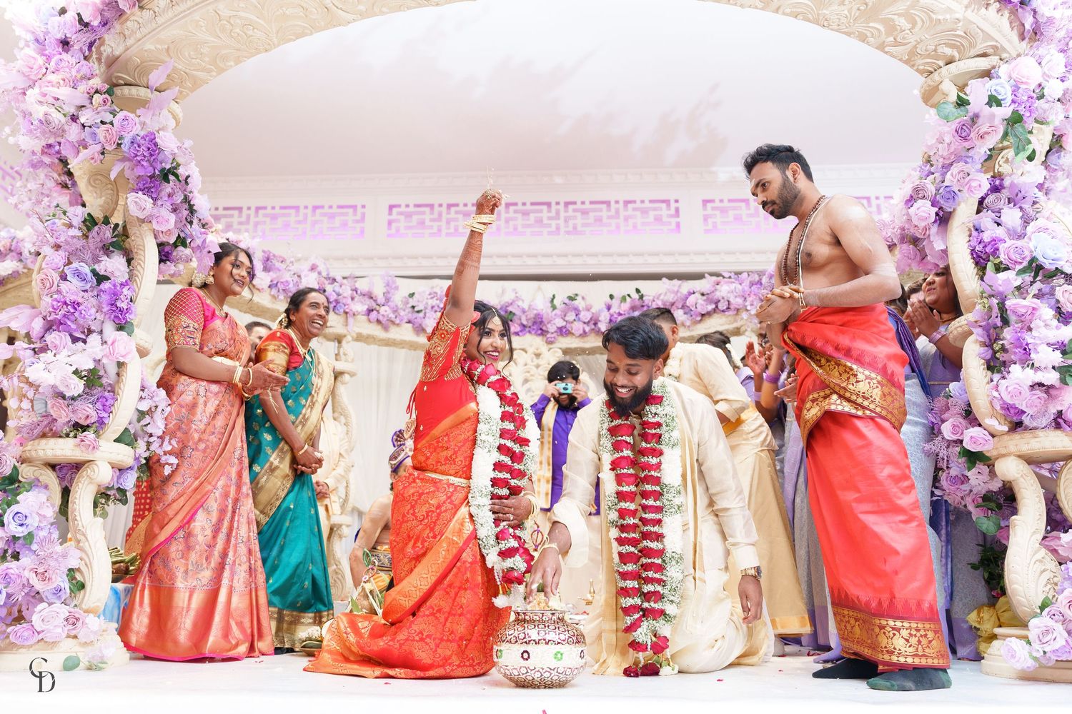 Festive wedding celebration under purple floral arch with guests in colorful traditional Indian attire.