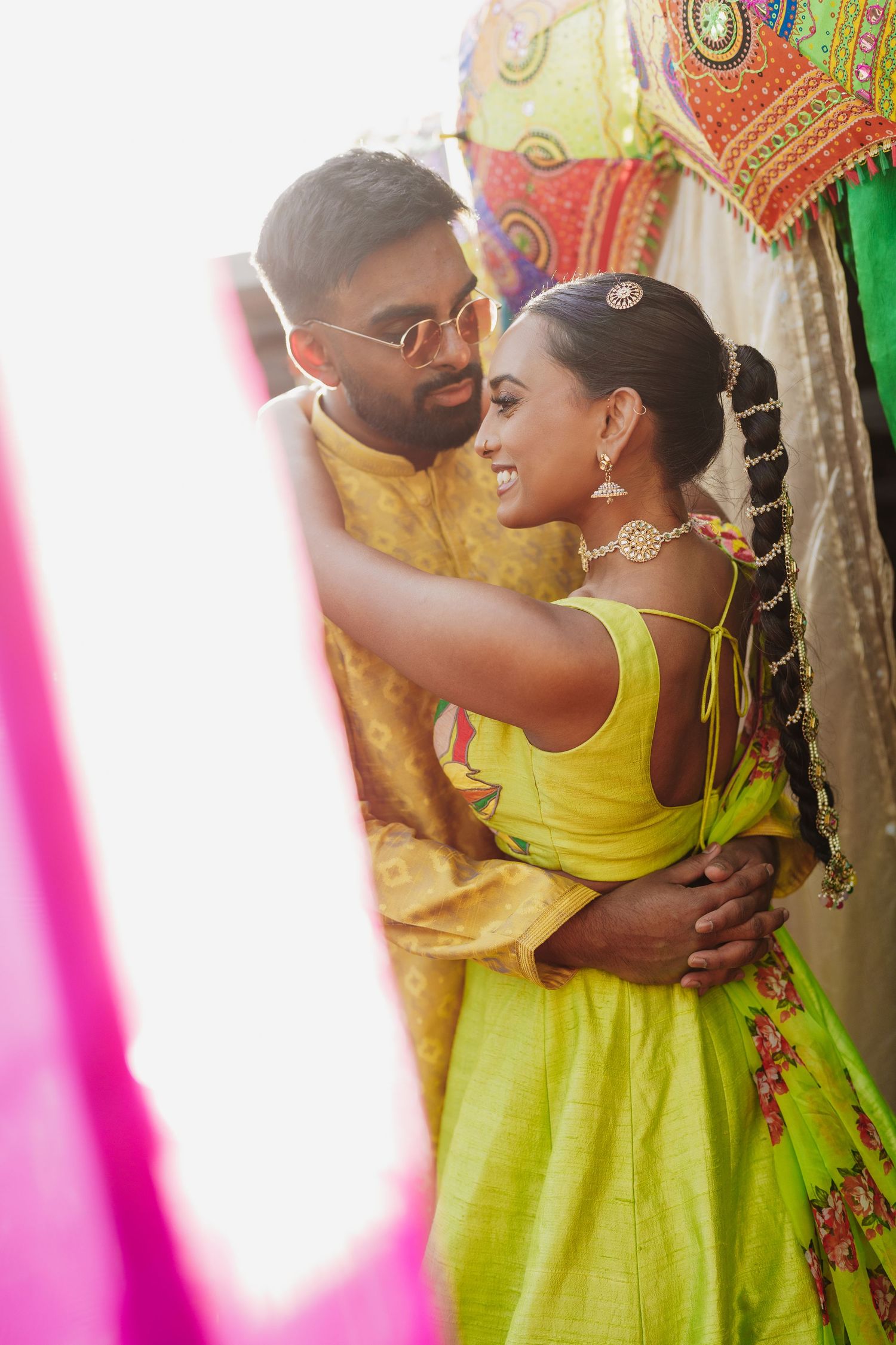 A couple in vibrant yellow and green traditional Indian attire embracing during a dance or celebration.