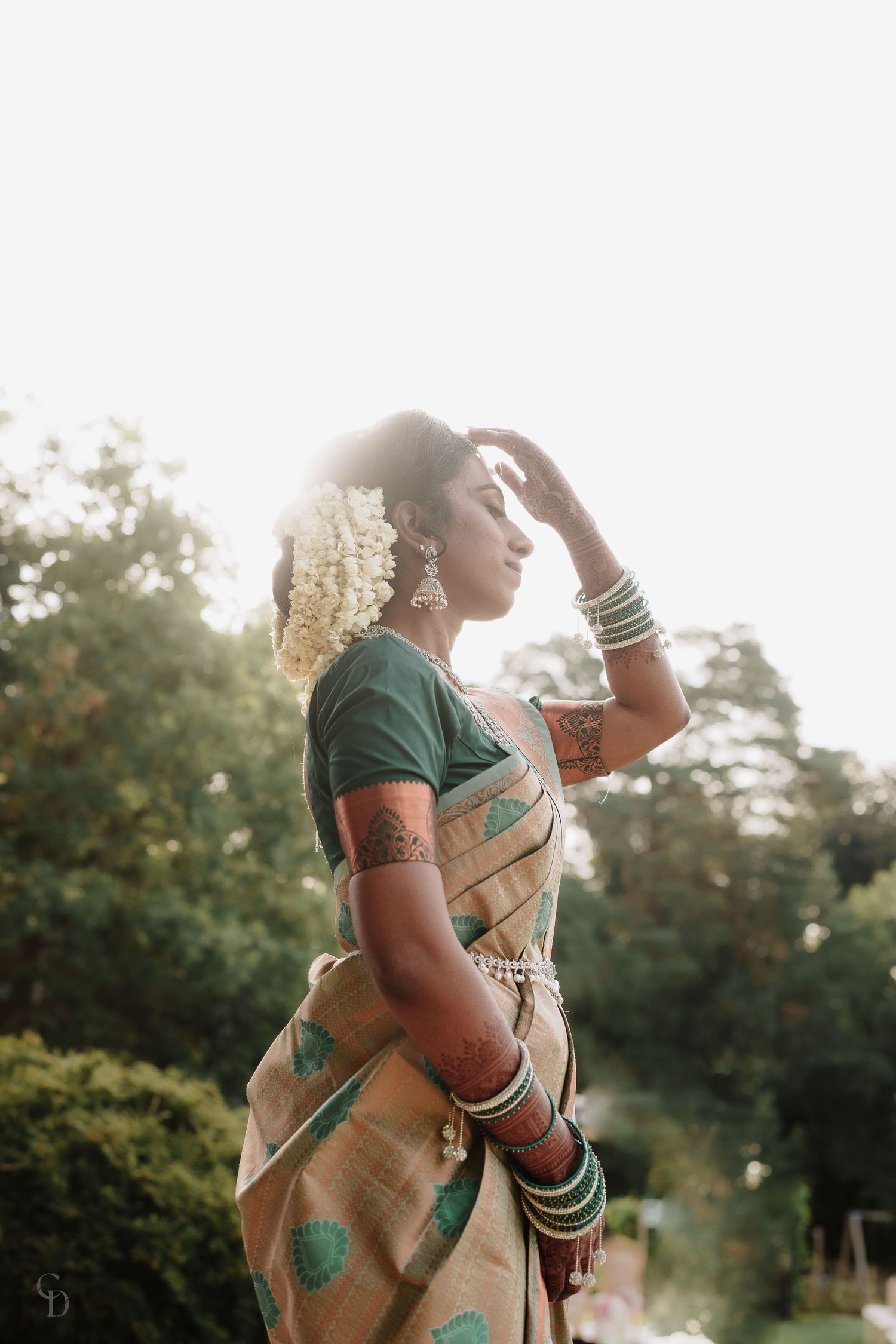 Traditional South Indian bride in green and beige saree with jasmine flowers and bangles at sunset.