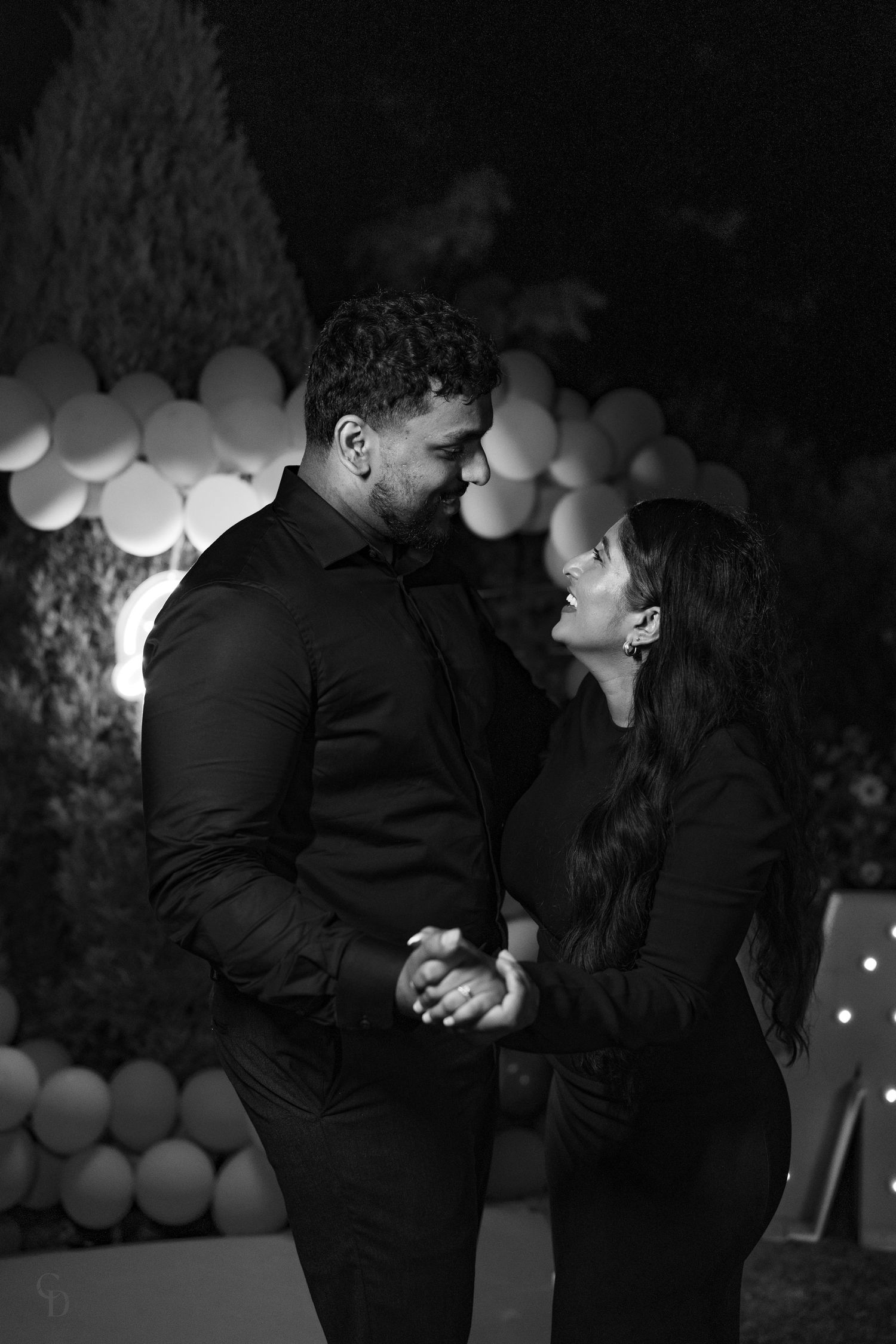 A black and white portrait with balloon decor showing a romantic moment between a couple.