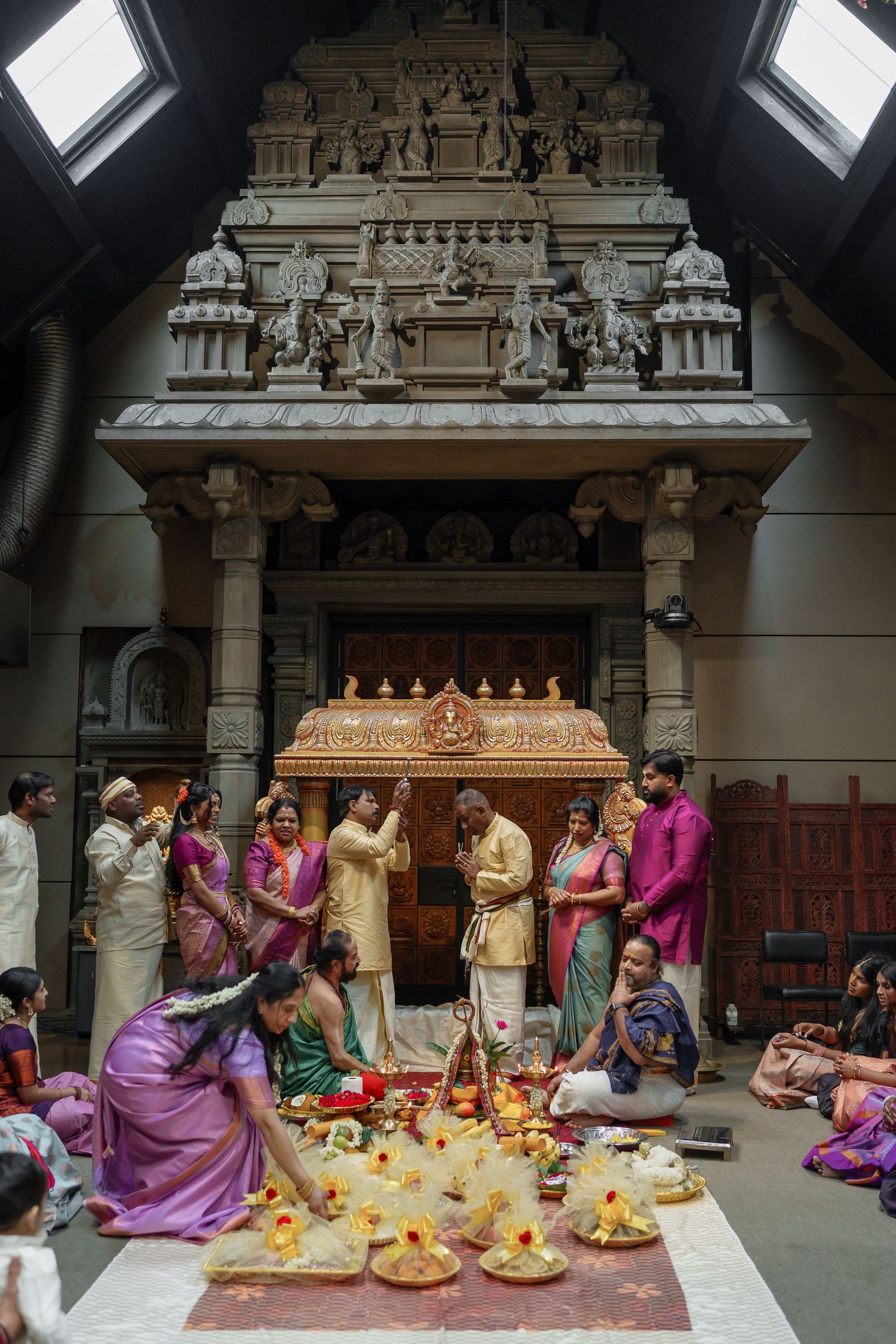 Traditional South Indian Hindu wedding ceremony at ornate temple with guests in colorful silk sarees and ritual offerings.