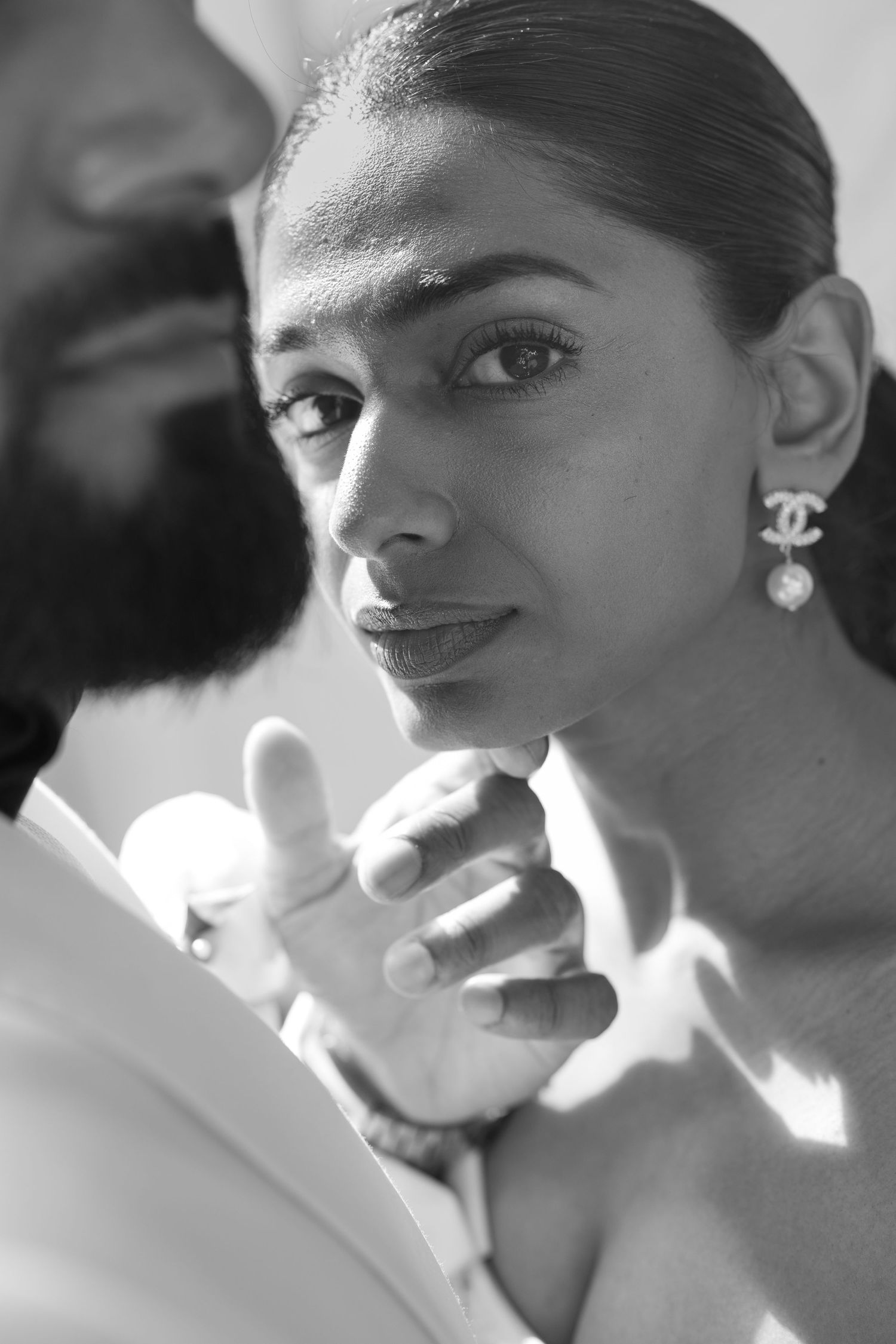A stunning black and white portrait showing elegant Chanel pearl earrings and sleek pulled back hair in soft lighting.