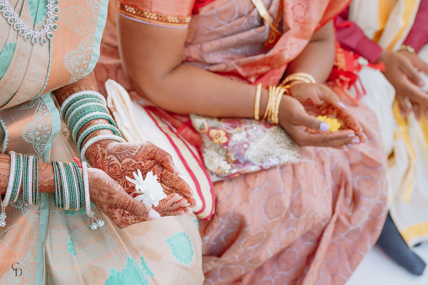 Close-up of hands with mehndi designs and turquoise bangles holding traditional items.