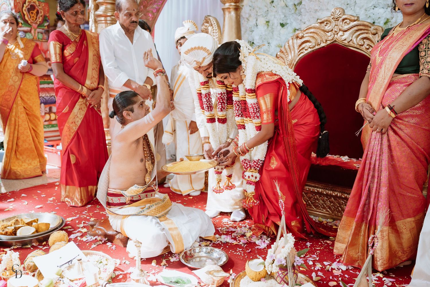 Traditional Hindu wedding ceremony with participants performing rituals on decorated floor.