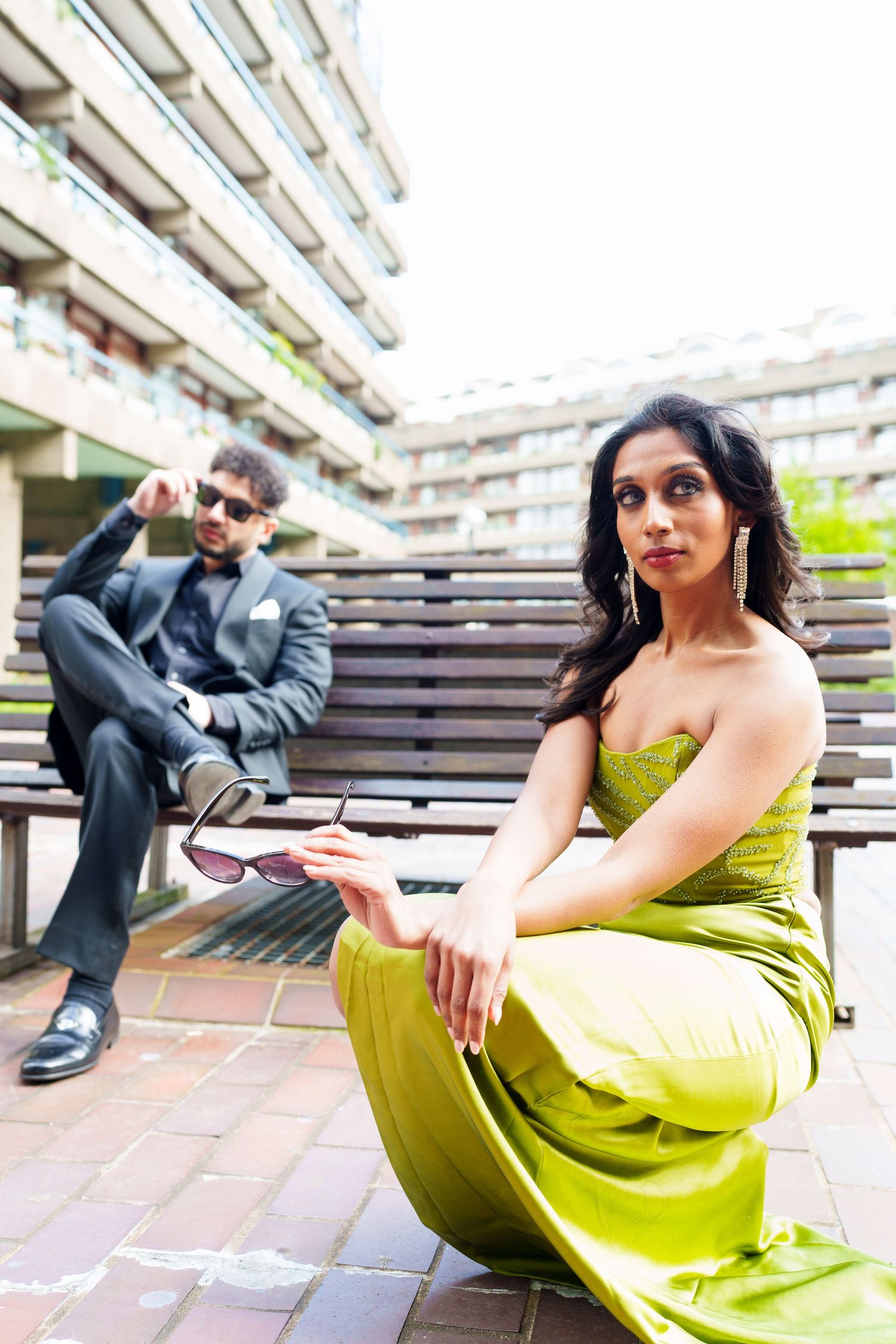 A stylish couple in formal wear posing on urban steps with architectural details in the background.