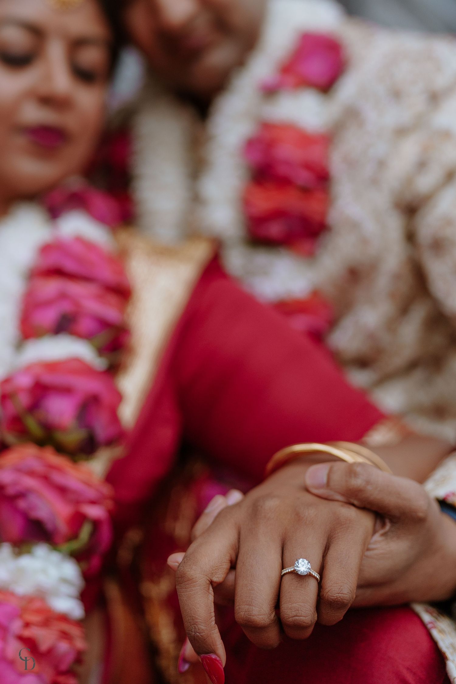 Close-up of hands with engagement ring and pink flower garlands.