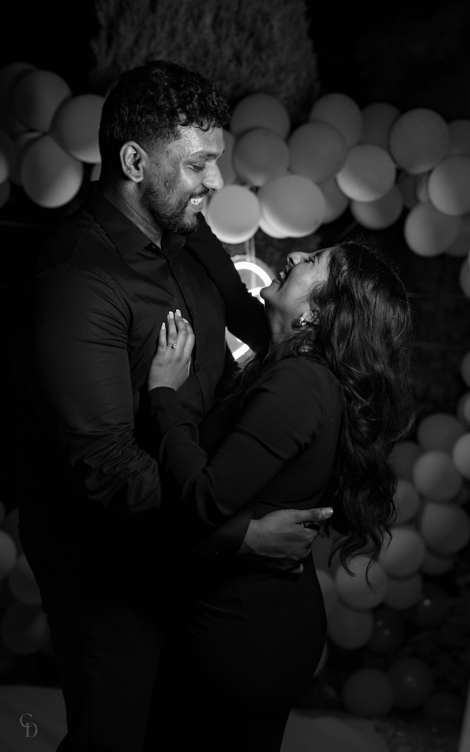 Black and white portrait of couple sharing intimate moment with balloon decor backdrop.