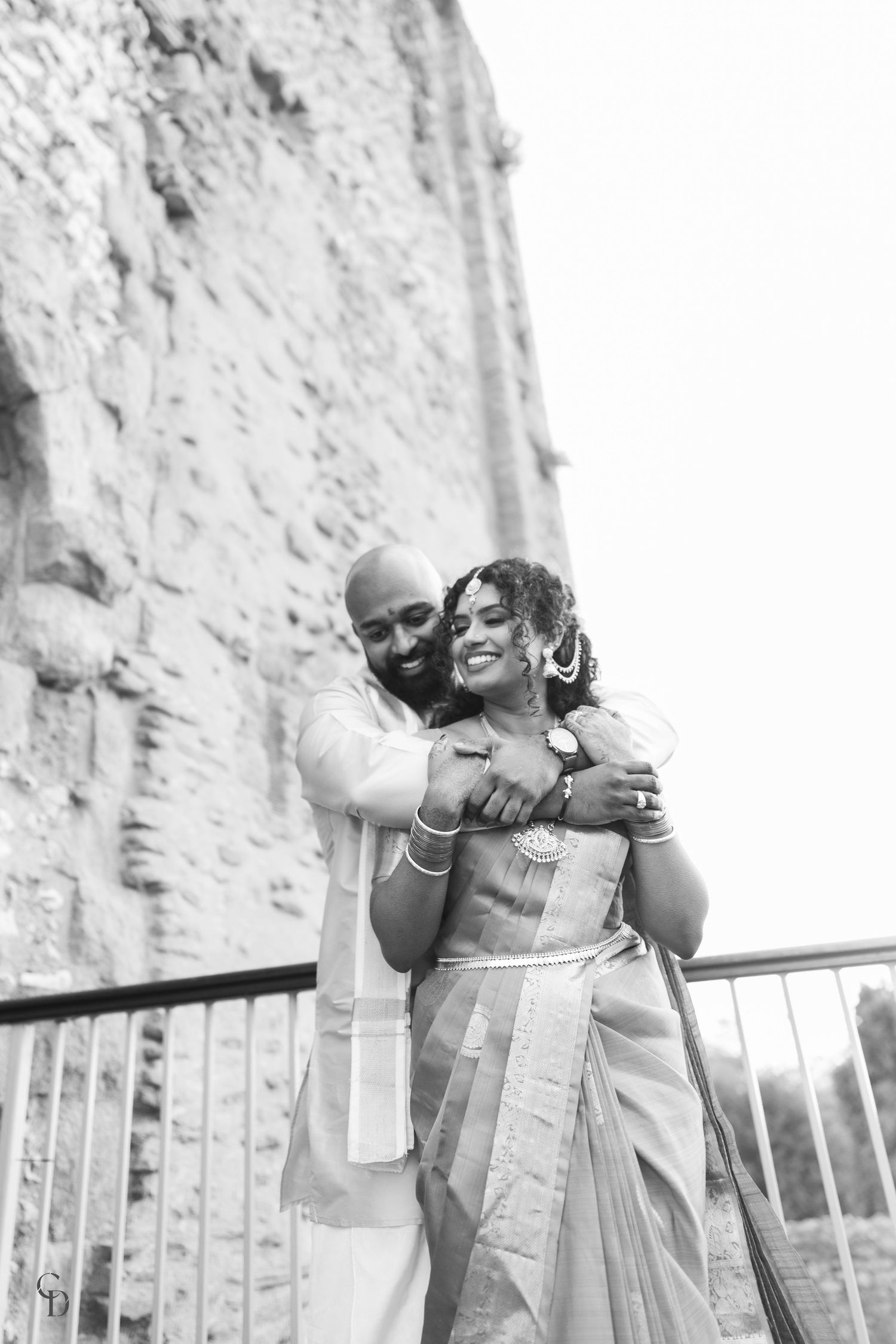 Black and white romantic portrait against stone wall showing traditional Indian wedding attire.