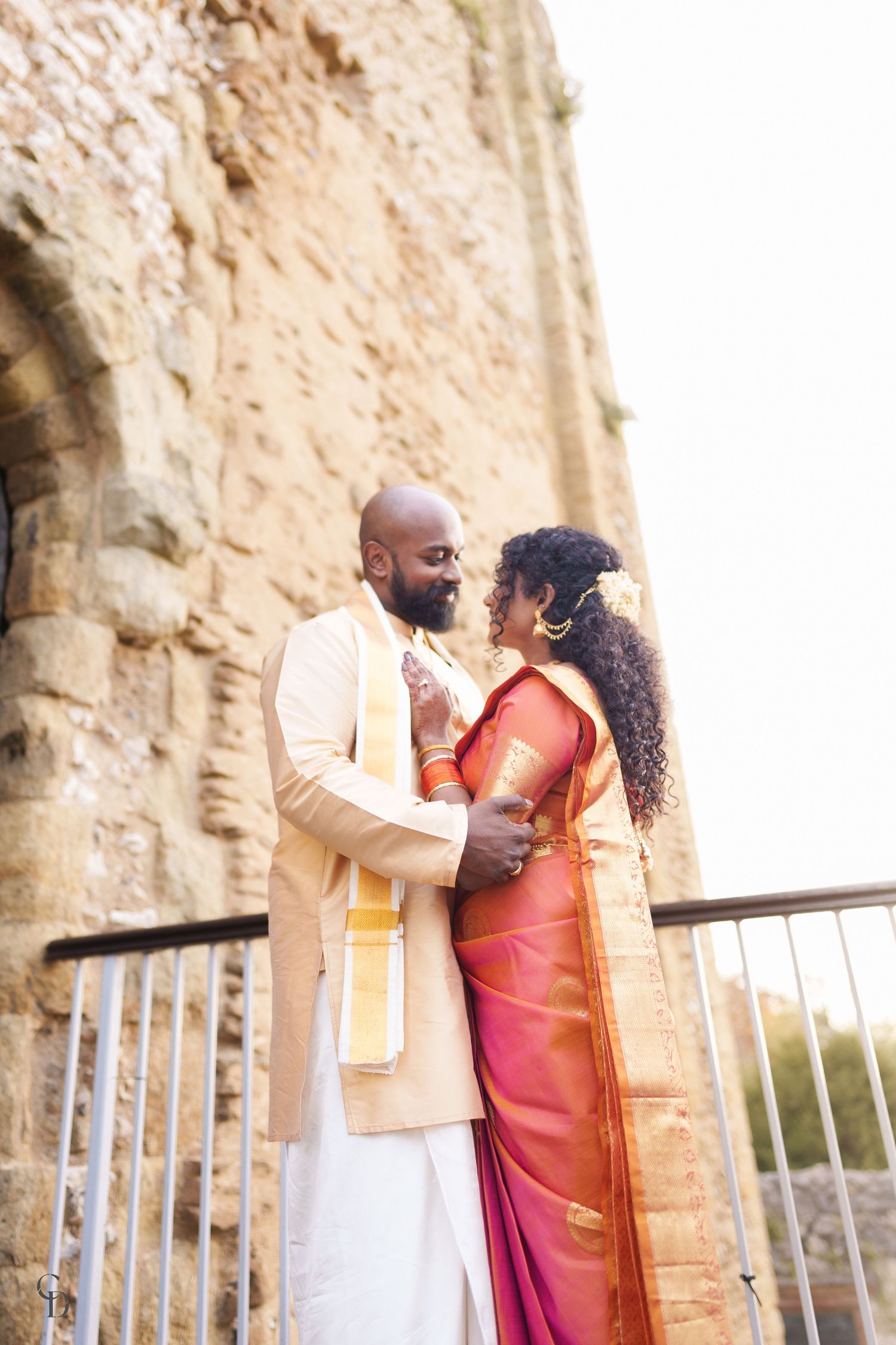 A romantic moment between newlyweds in traditional South Asian attire against historic stone architecture.