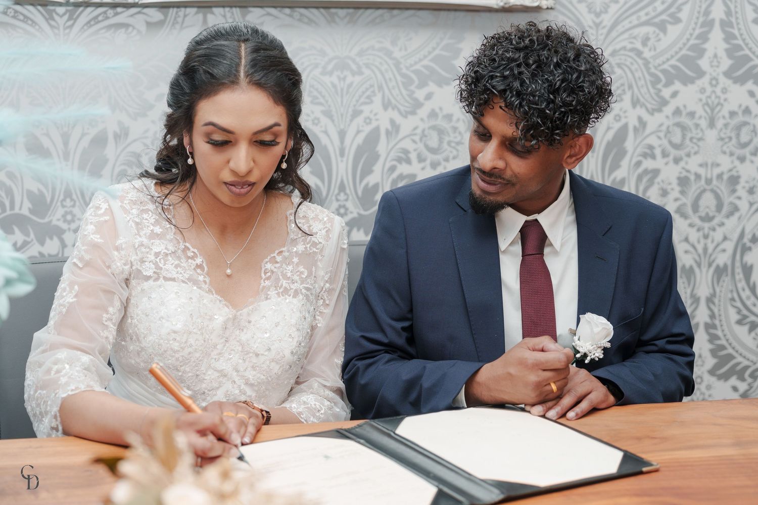 Bride and groom signing official wedding documents at decorated registration table.