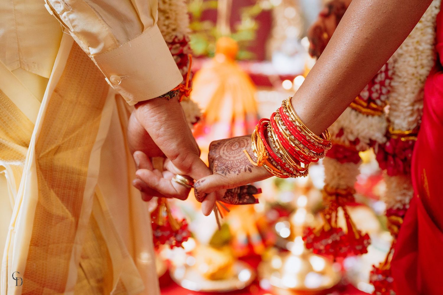 Traditional Indian wedding ritual showing hands adorned with mehndi and red bangles.