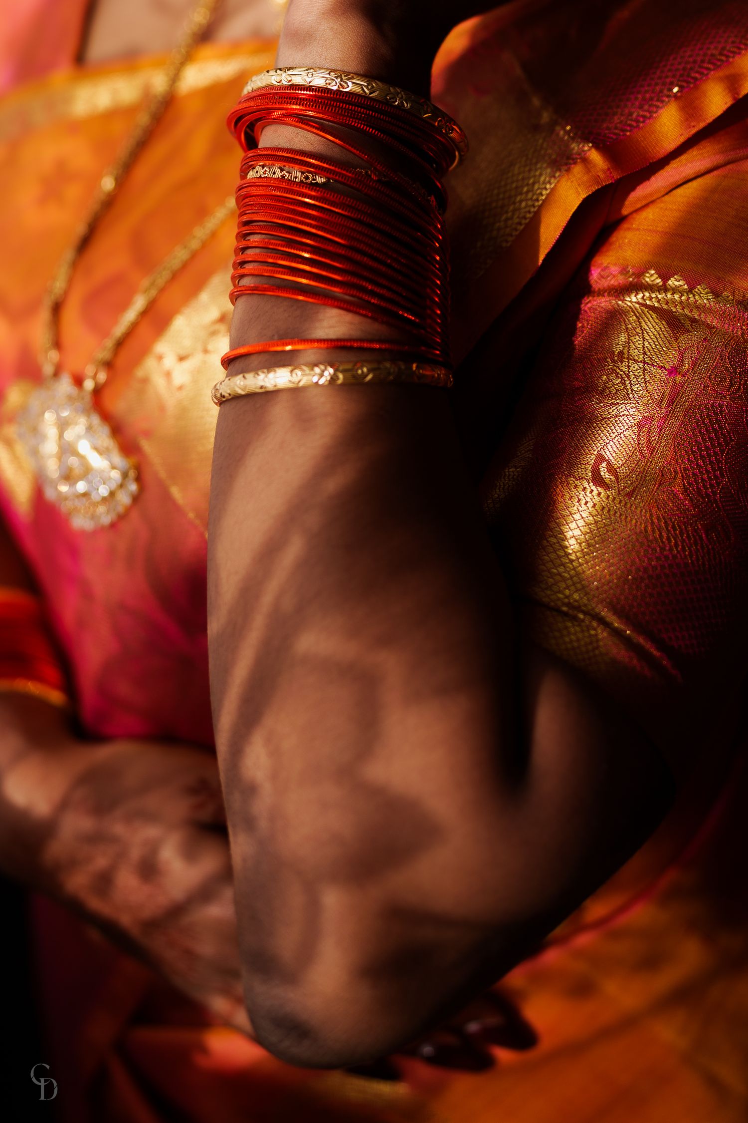 Close-up of traditional red wedding bangles and jewelry against rich orange silk fabric.