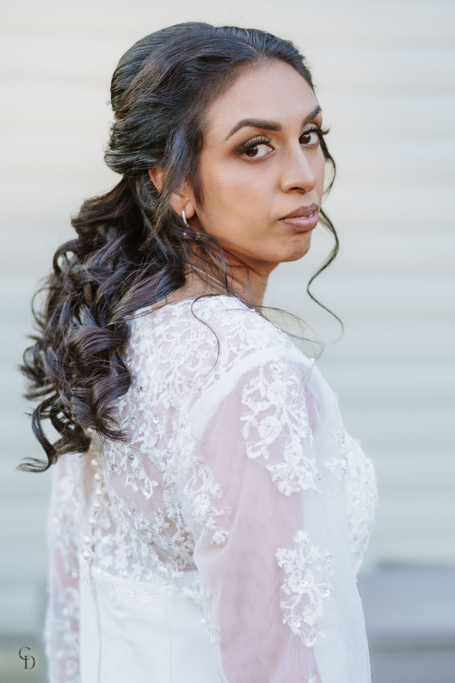 Bride in elegant lace wedding dress with curled hair styled in a romantic half-up look.
