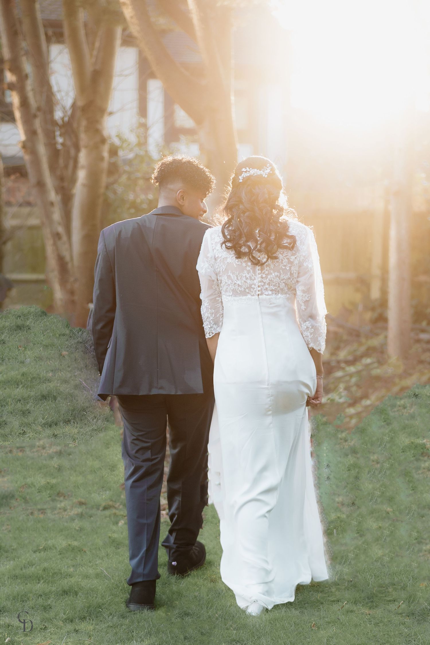Newlyweds walking together at sunset through garden path in wedding attire.